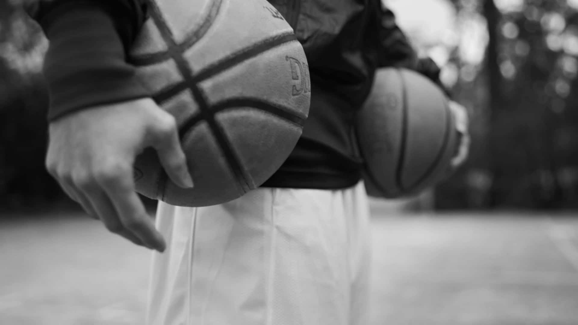 1080p Basketball 桌布 壁紙 — 黑白特寫，一個人拿著兩個籃球，背景是模糊的戶外。