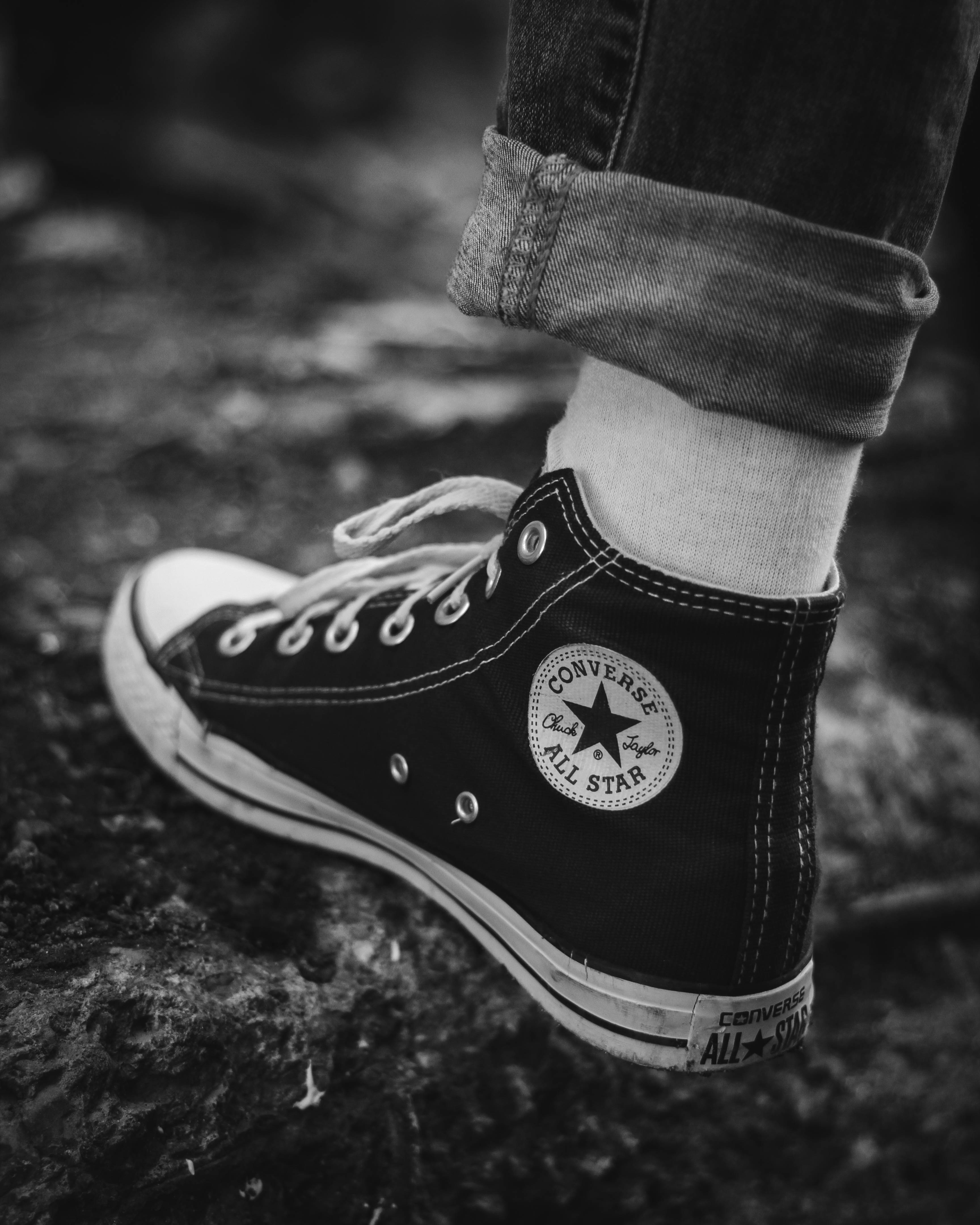 Converse 桌布 壁紙 — 黑白特寫，一個人的腳穿著經典 Converse All Star 高筒運動鞋，站在有紋理的石頭表面上。