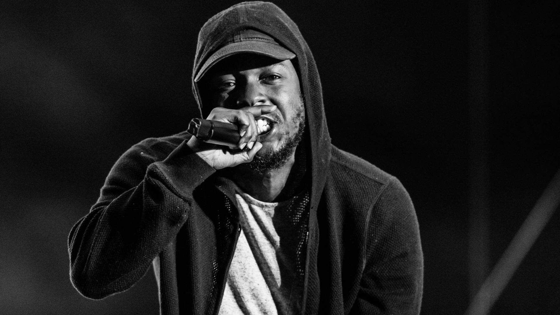 Kendrick 桌布 壁紙 — 黑白特寫，一名男饒舌歌手在舞台燈光下熱情地對著麥克風表演。