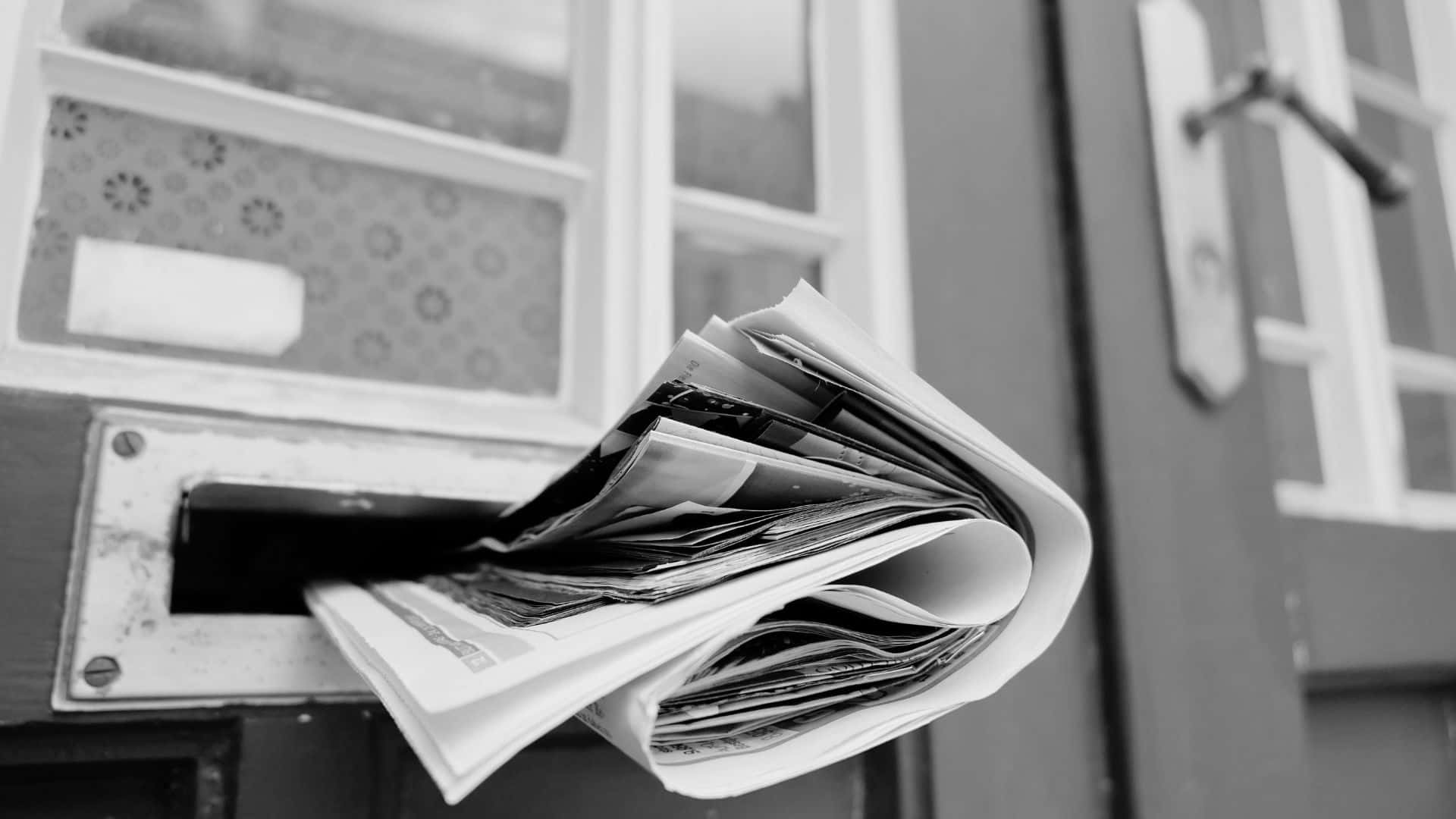 Black And White Newspaper 桌布 壁紙 — 黑白特寫，報紙從附在木門上的風化郵箱中溢出。
