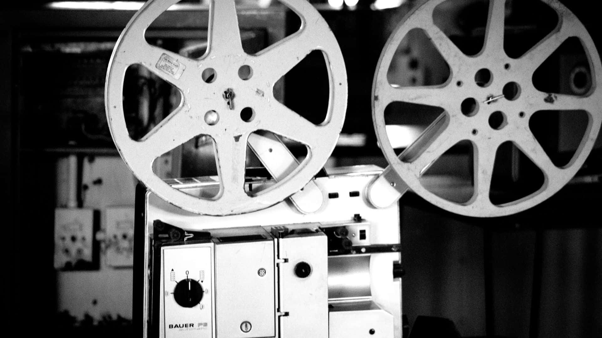 Black And White Movie 桌布 壁紙 — 黑白特寫，展示在昏暗房間中的復古電影放映機捲軸，帶有詳細的機械部件。