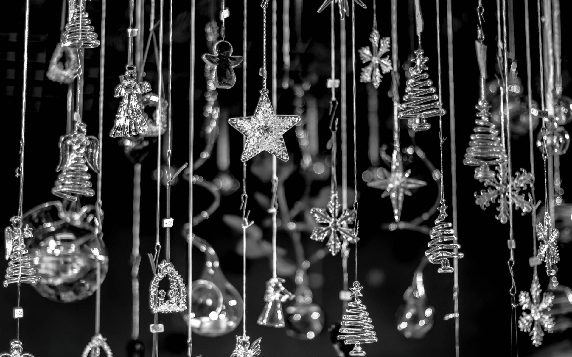 Black Christmas 桌布 壁紙 — 黑白特寫，懸掛的玻璃聖誕裝飾品，形狀像星星、樹木、雪花和天使，背景為黑暗模糊。