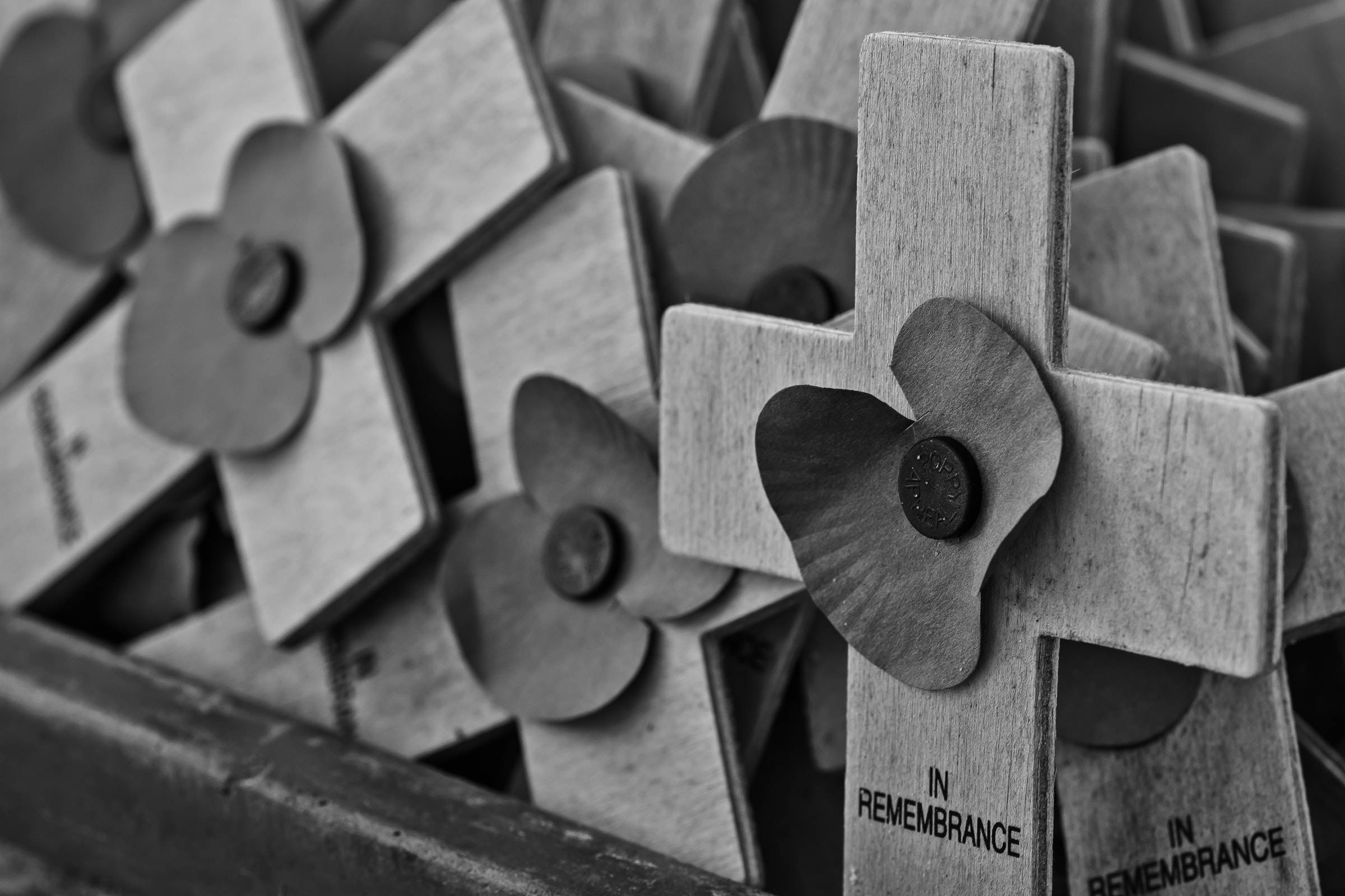 Remembrance 桌布 壁紙 — 黑白特寫，木製十字架上裝飾著罌粟花，刻有「IN REMEMBRANCE」的莊嚴紀念展示。