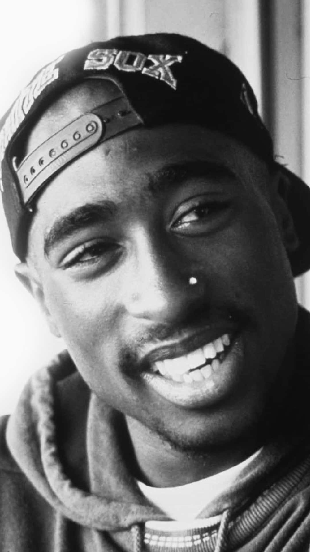 一名微笑男子戴著向後帽子及連帽衫，有鼻環。 — Tupac GIF 壁紙