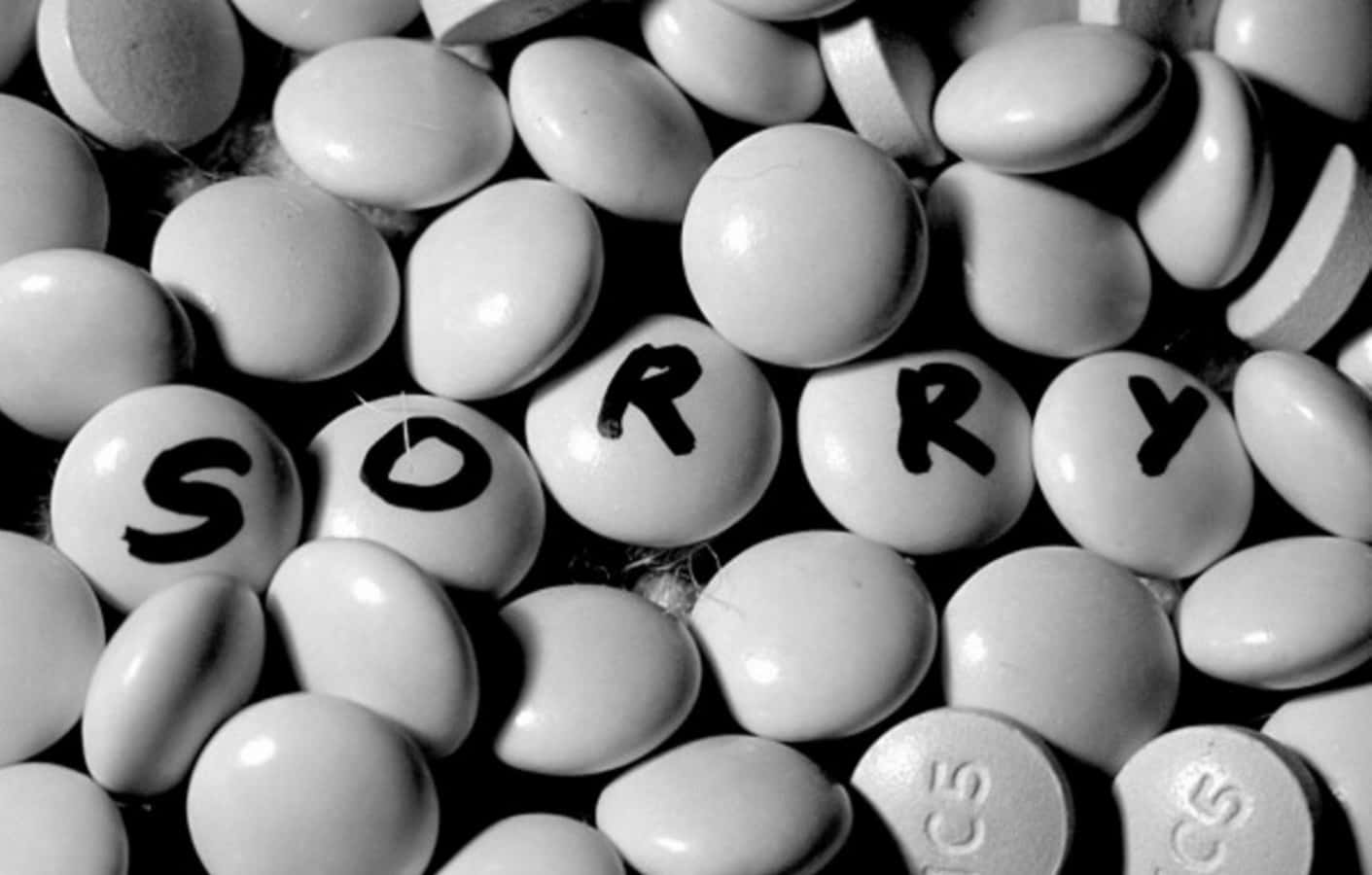 糖果 桌布 壁紙 — 黑白特寫藥丸，部分藥丸上手寫「sorry」一詞，傳達遺憾或道歉。