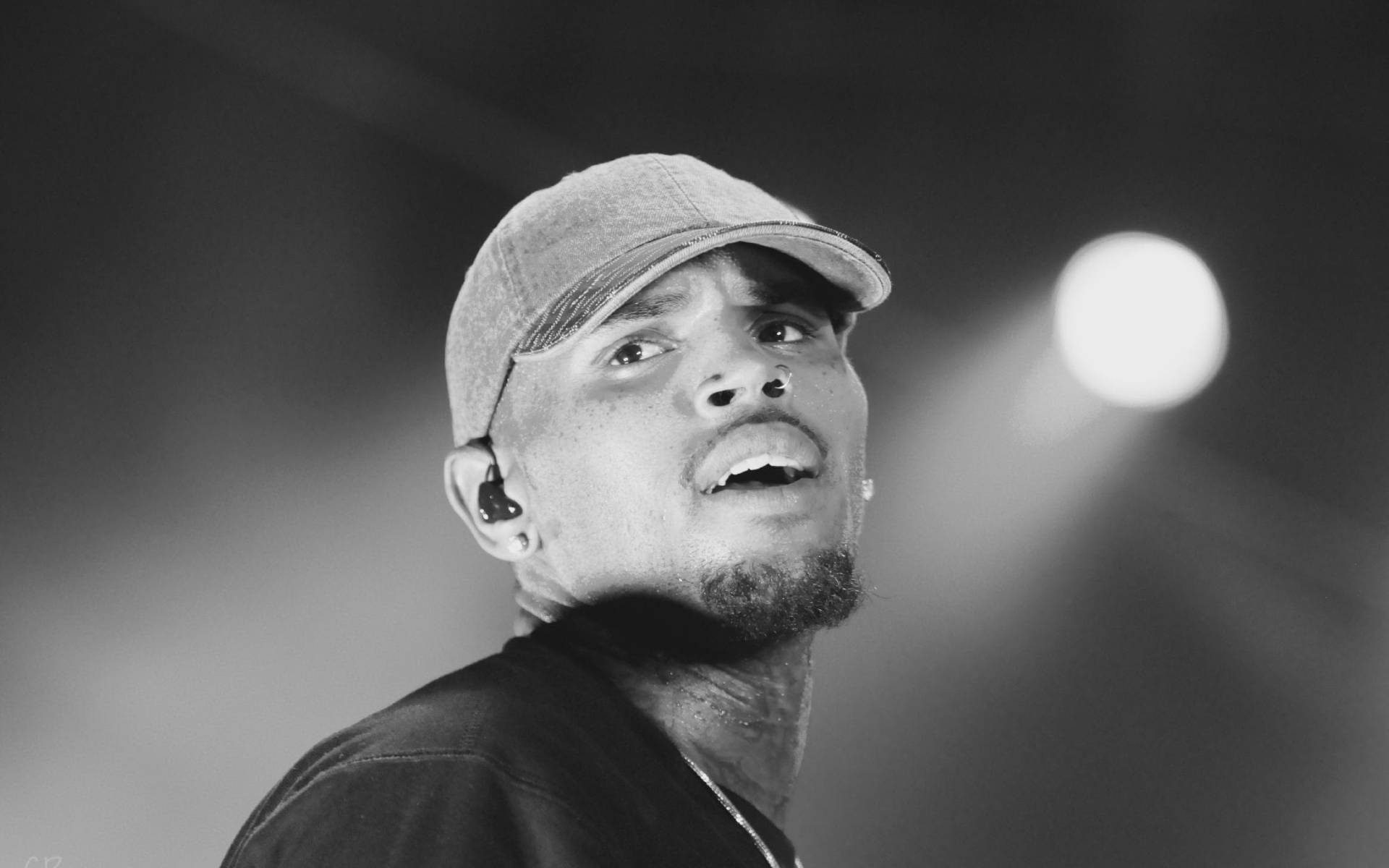 Chris Brown 桌布 壁紙 — 黑白特寫鏡頭，一名戴著帽子的男表演者在舞台燈光下熱情演唱。