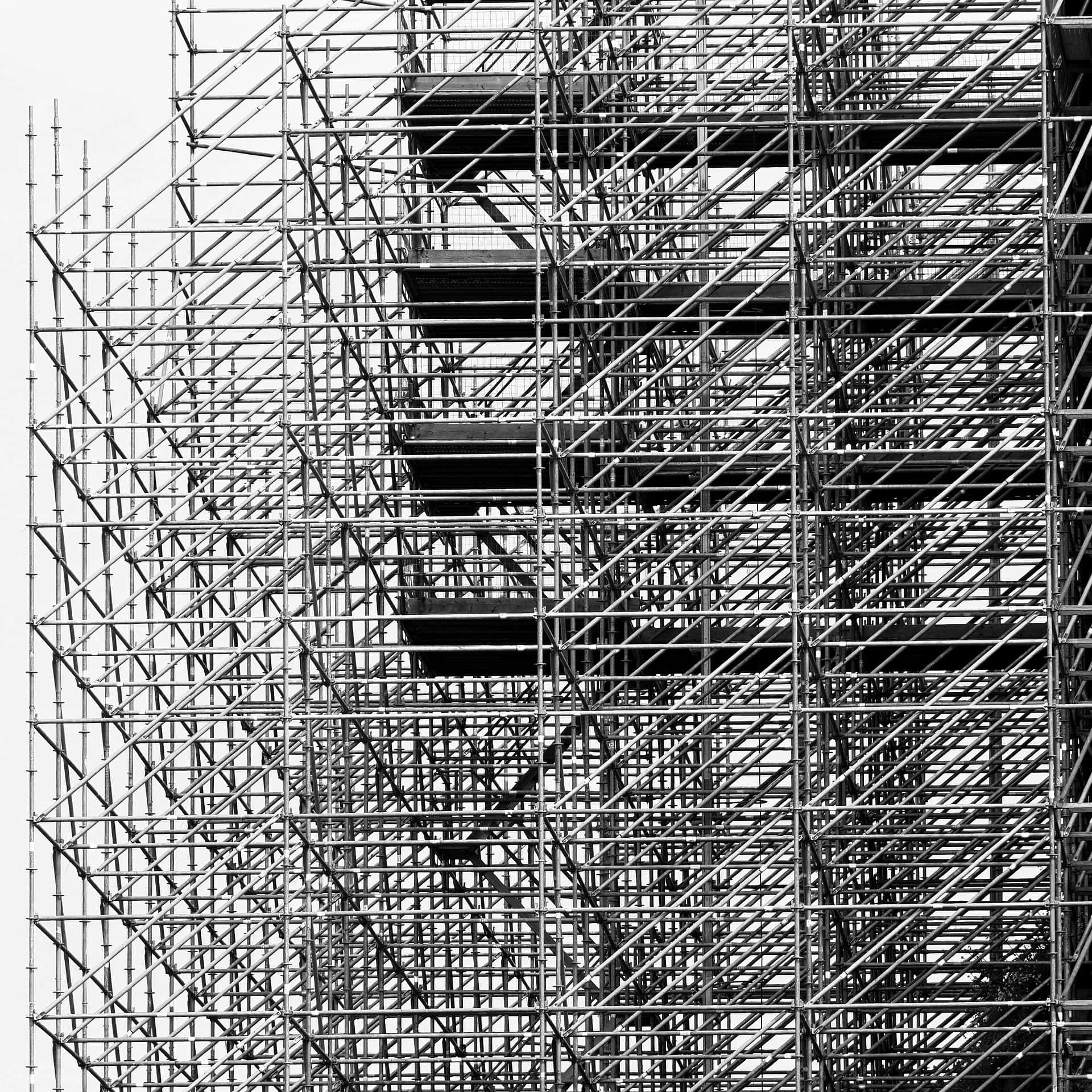Scaffolding 桌布 壁紙 — 黑白特寫鏡頭，呈現複雜的金屬鷹架在明亮天空下形成幾何格狀結構。