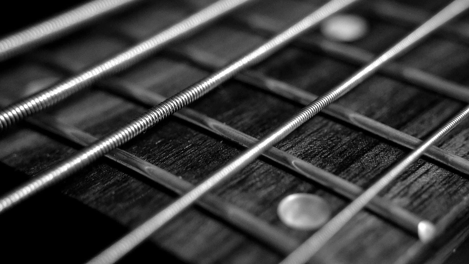 Black And White Guitar 桌布 壁紙 — 黑白特寫鏡頭，清晰對焦於穿過帶有金屬琴格的木製指板的吉他弦。