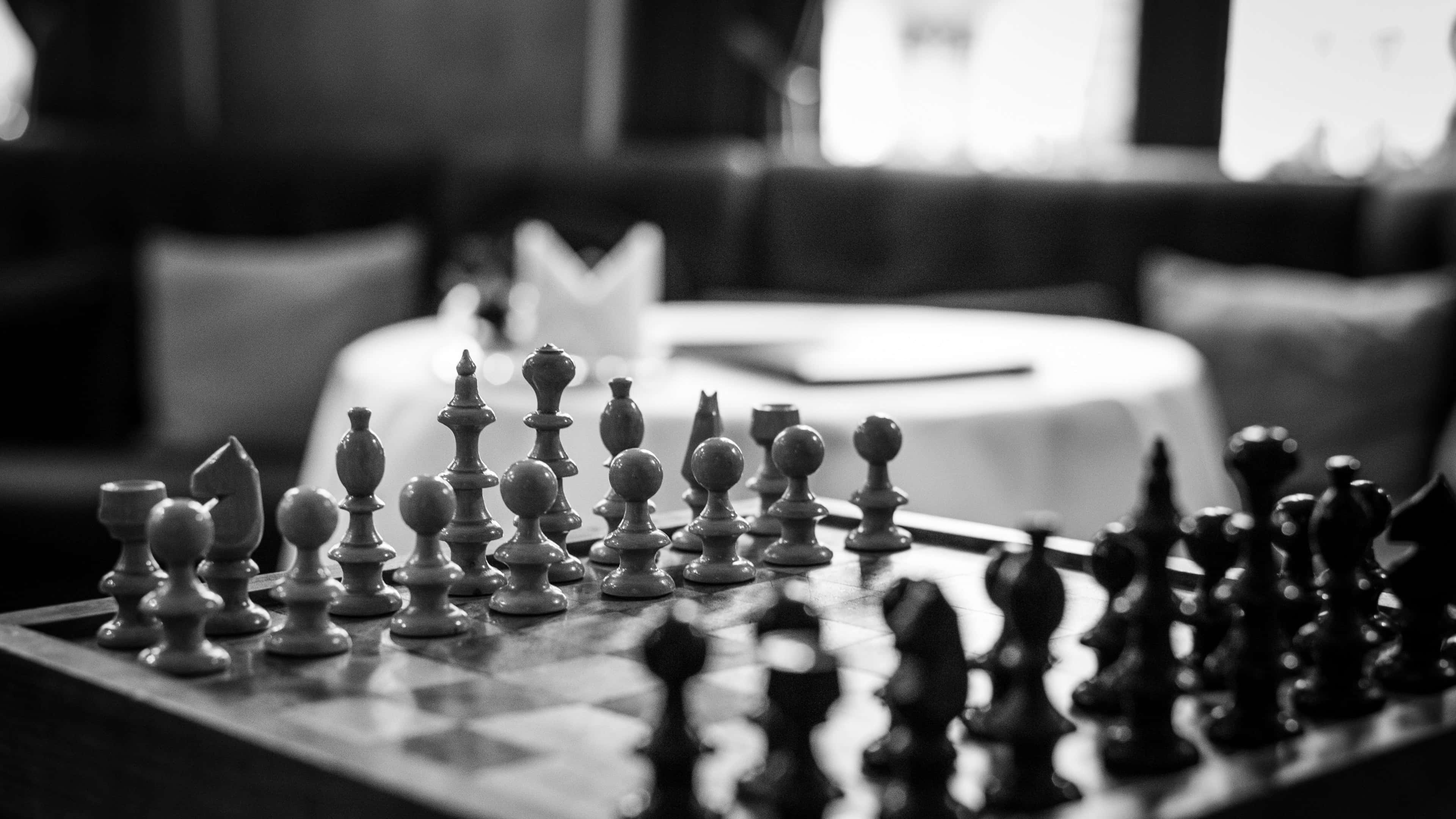 Black And White Chess 桌布 壁紙 — 黑白特寫鏡頭，聚焦於棋盤上的棋子，背景是模糊的餐廳餐桌。