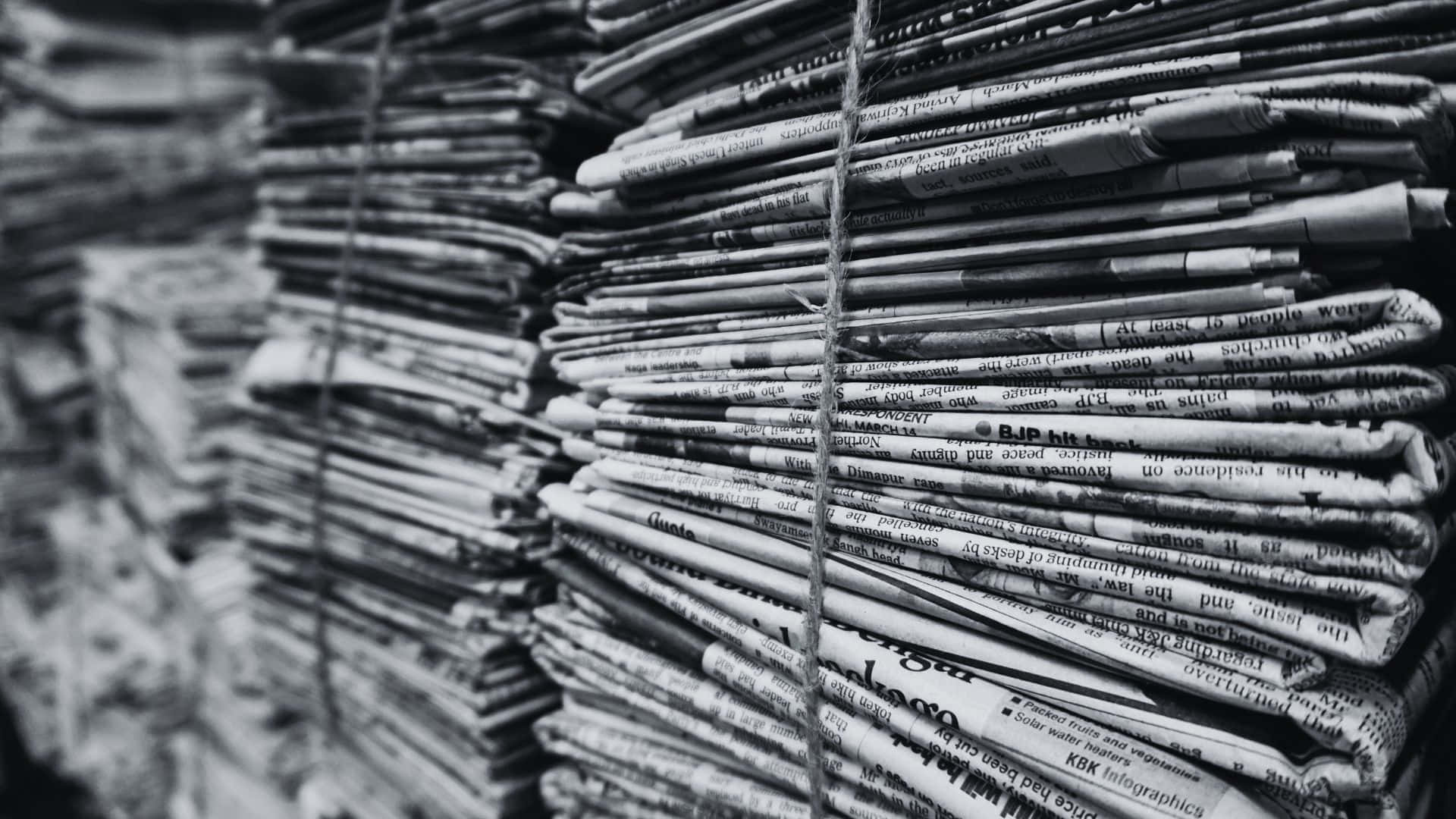 Black And White Newspaper 桌布 壁紙 — 黑白相間的捆綁報紙堆，可見標題和文字，營造出有紋理的都市檔案。