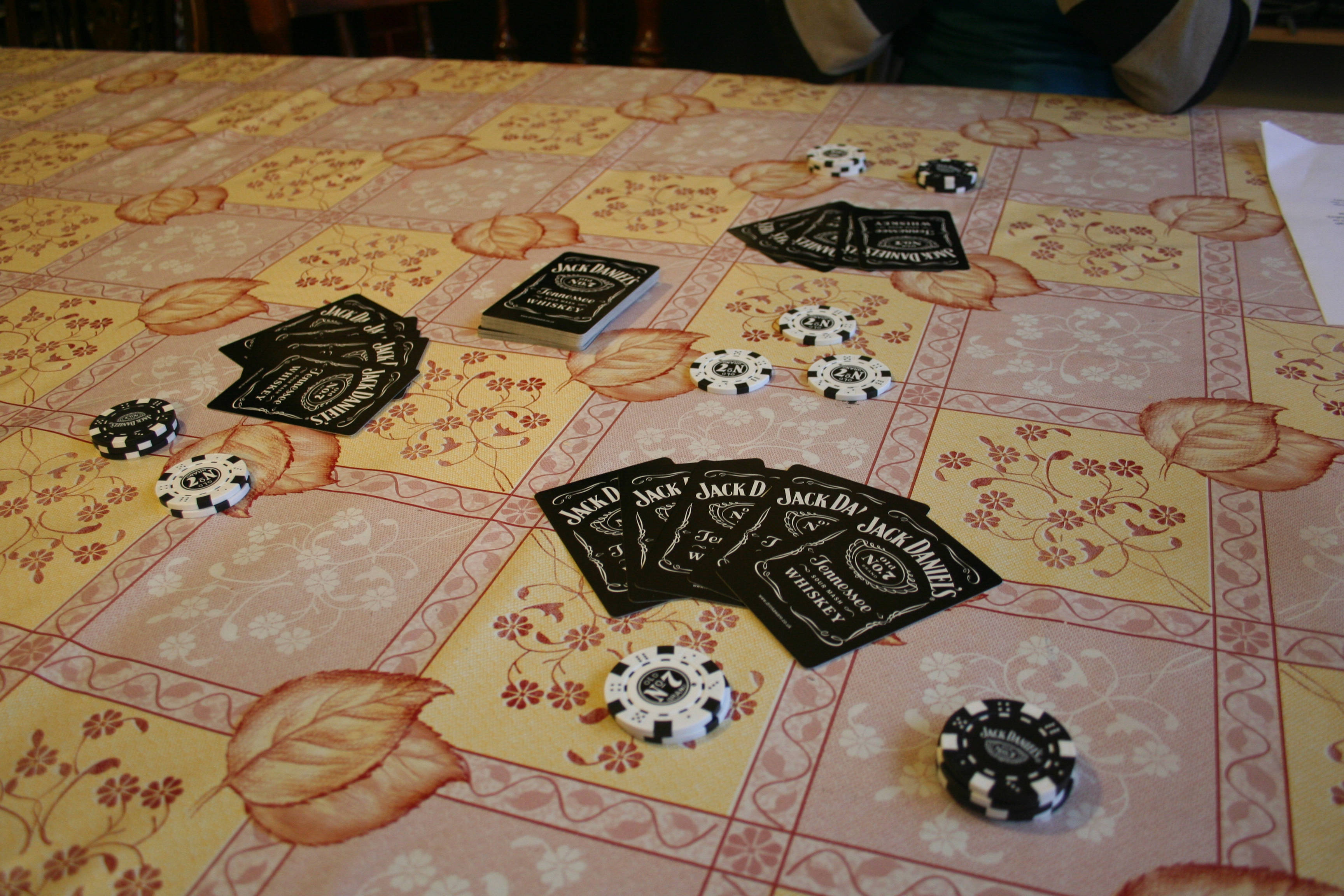 Cards 桌布 壁紙 — 黑白籌碼和Jack Daniel's撲克牌散落在花卉圖案的桌布上。