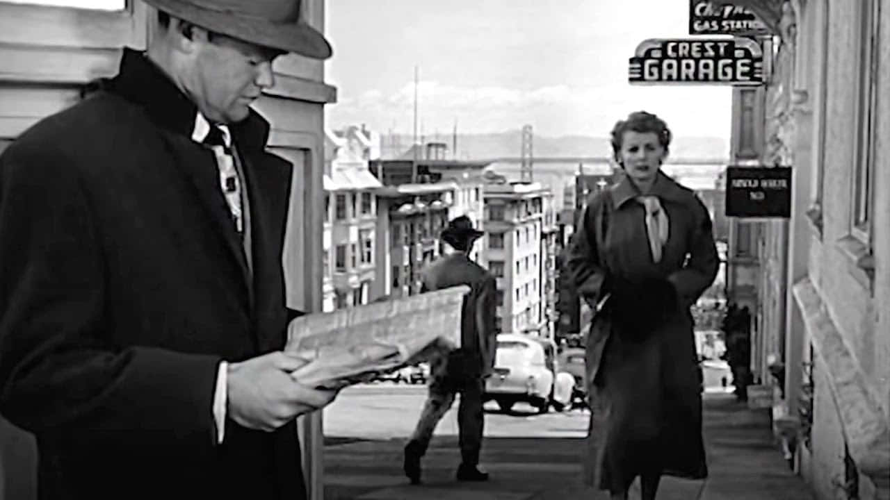 Film Noir 桌布 壁紙 — 黑白街景，一名戴帽男子正在閱讀報紙，一名女子走過「Crest Garage」標誌。