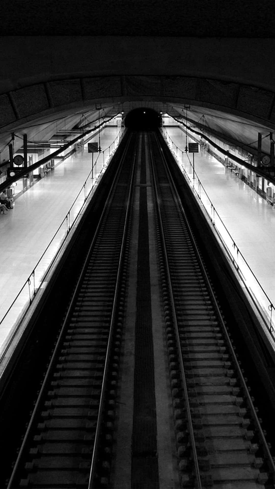 Black And White iPhone 桌布 壁紙 — 黑白鮮明的視角，向下望入空無一人的地鐵軌道，通向拱形車站天花板下的黑暗隧道。