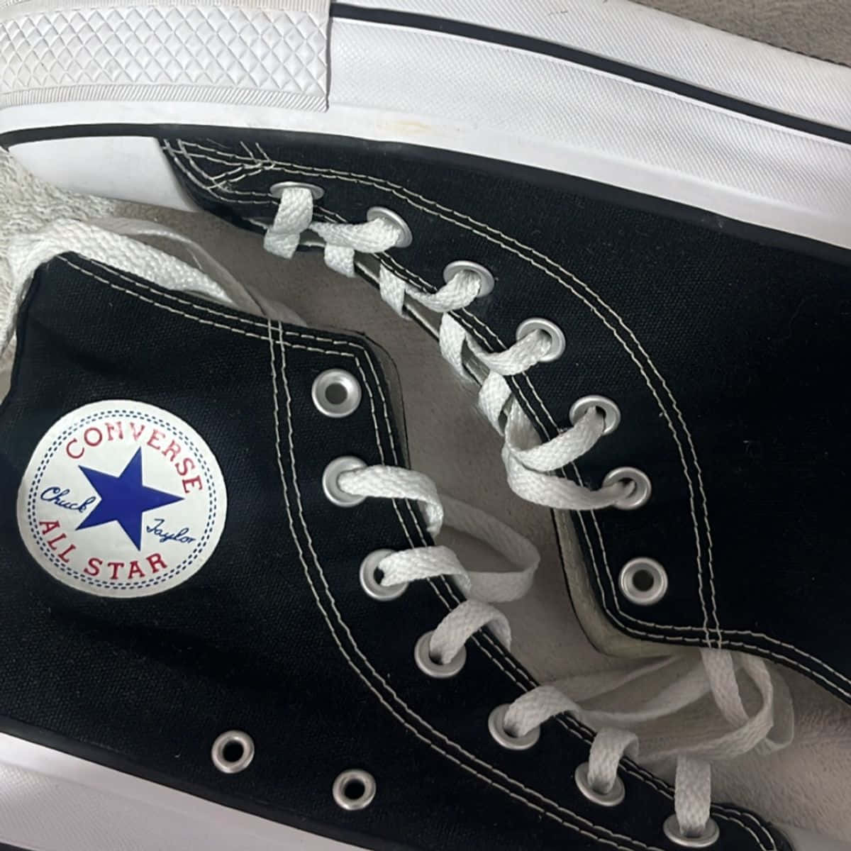 Converse 桌布 壁紙 — 黑色 Converse Chuck Taylor All Star 運動鞋特寫，配有白色鞋帶和縫線，背景為中性色調。