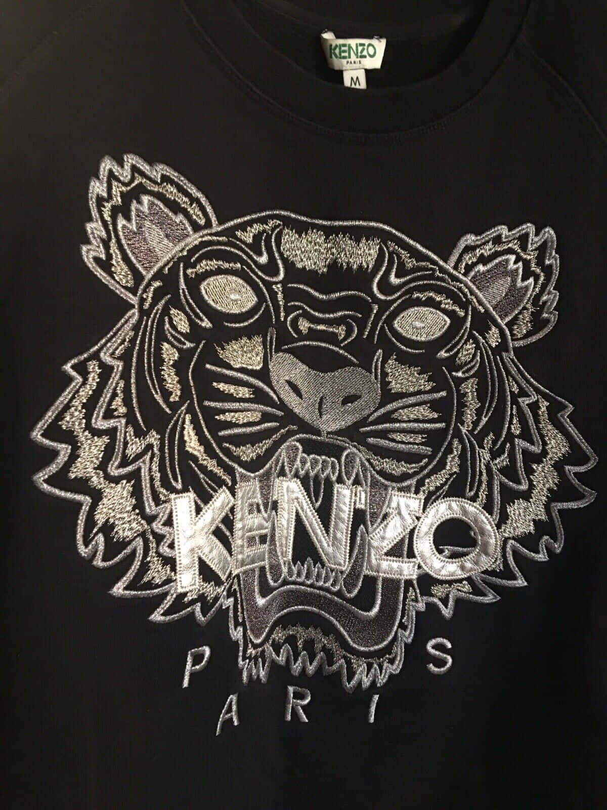 Designer Logo 桌布 壁紙 — 黑色 Kenzo 連帽衫特寫，帶有精緻的銀色刺繡老虎頭標誌，下方有「KENZO PARIS」字樣。