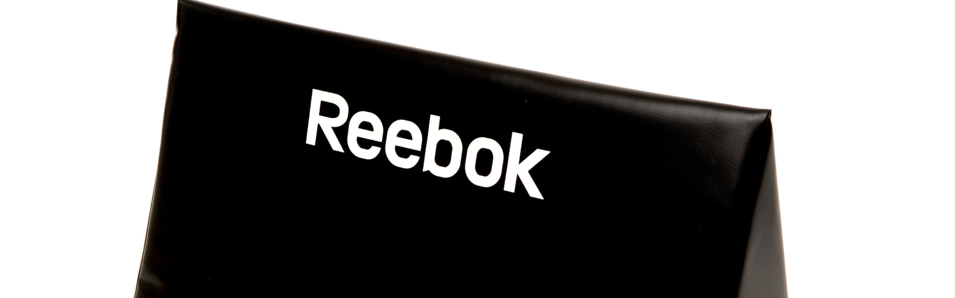Reebok 桌布 壁紙 — 黑色 Reebok 品牌拳擊靶墊的特寫，帶有粗體白色標誌，背景為純白色。