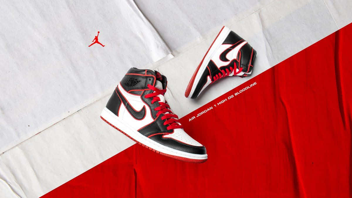 Air Jordan 1 桌布 壁紙 — 黑色、白色和紅色的 Air Jordan 1 高筒鞋放置在對角線分割的紅色和白色布料背景上，並帶有品牌標誌。