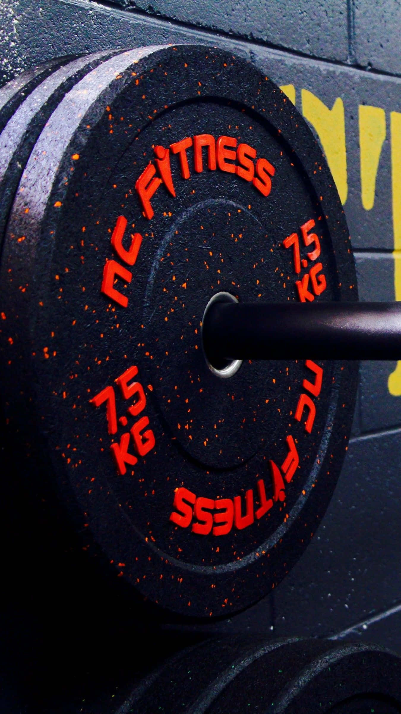 桌布 壁紙 — 黑色7.5公斤槓鈴片特寫，帶有紅色'NC FITNESS'文字和斑點，背景為深色健身房牆壁。