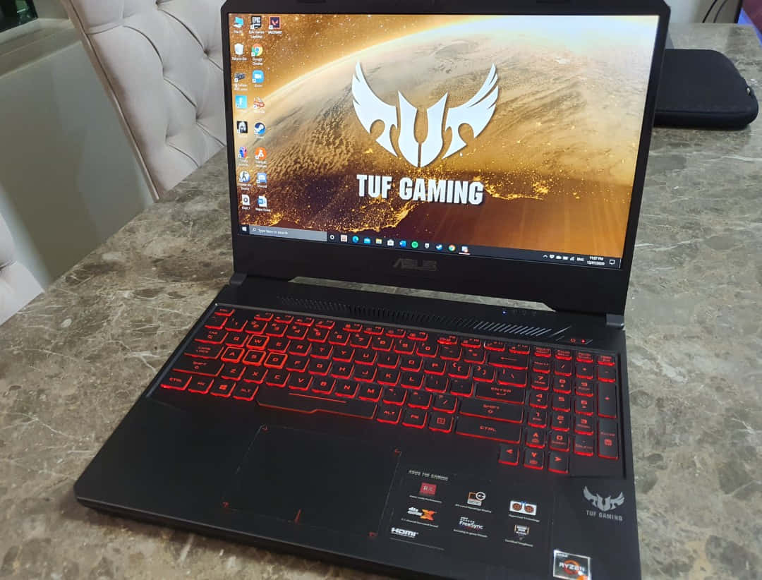 ASUS 桌布 壁紙 — 黑色ASUS TUF Gaming筆記型電腦，配備紅色發光背光鍵盤，打開放在大理石檯面上，顯示熾熱星球壁紙。