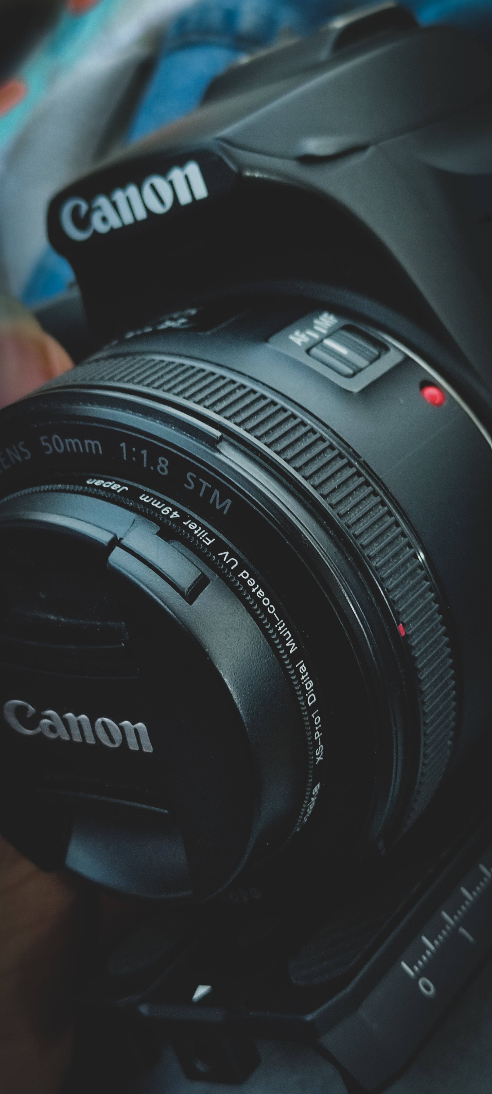 相機 桌布 壁紙 — 黑色Canon DSLR相機特寫，帶有50mm鏡頭蓋，背景模糊多彩。