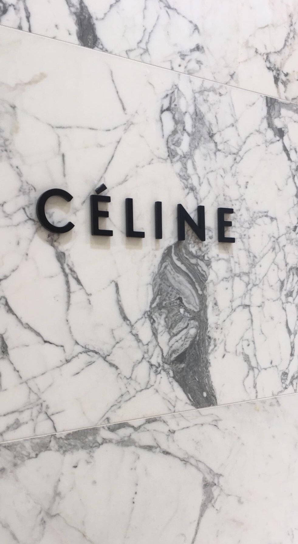 品牌 桌布 壁紙 — 黑色Celine標誌字母安裝在白色和灰色紋理大理石牆上，線條簡潔現代。