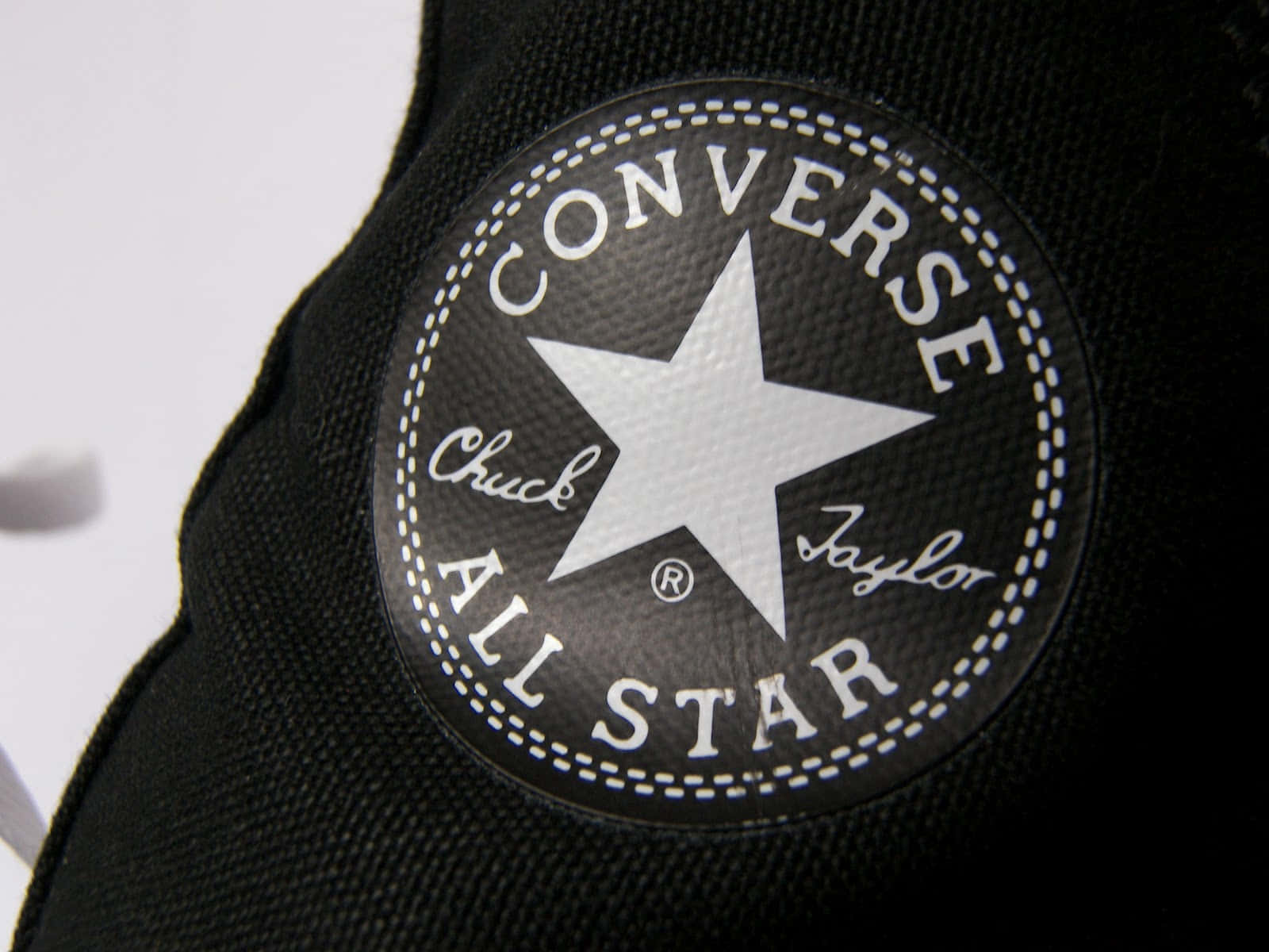 Converse 標誌 桌布 壁紙 — 黑色Converse All Star標誌布章近照，上有白色星星及縫線，位於帆布鞋上。