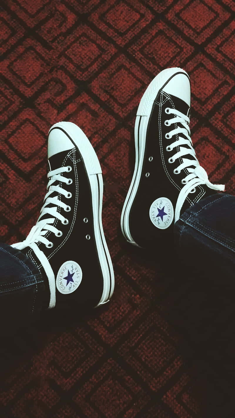 Converse 桌布 壁紙 — 黑色Converse運動鞋，白色鞋帶和星星標誌，放在紅色圖案地毯上。