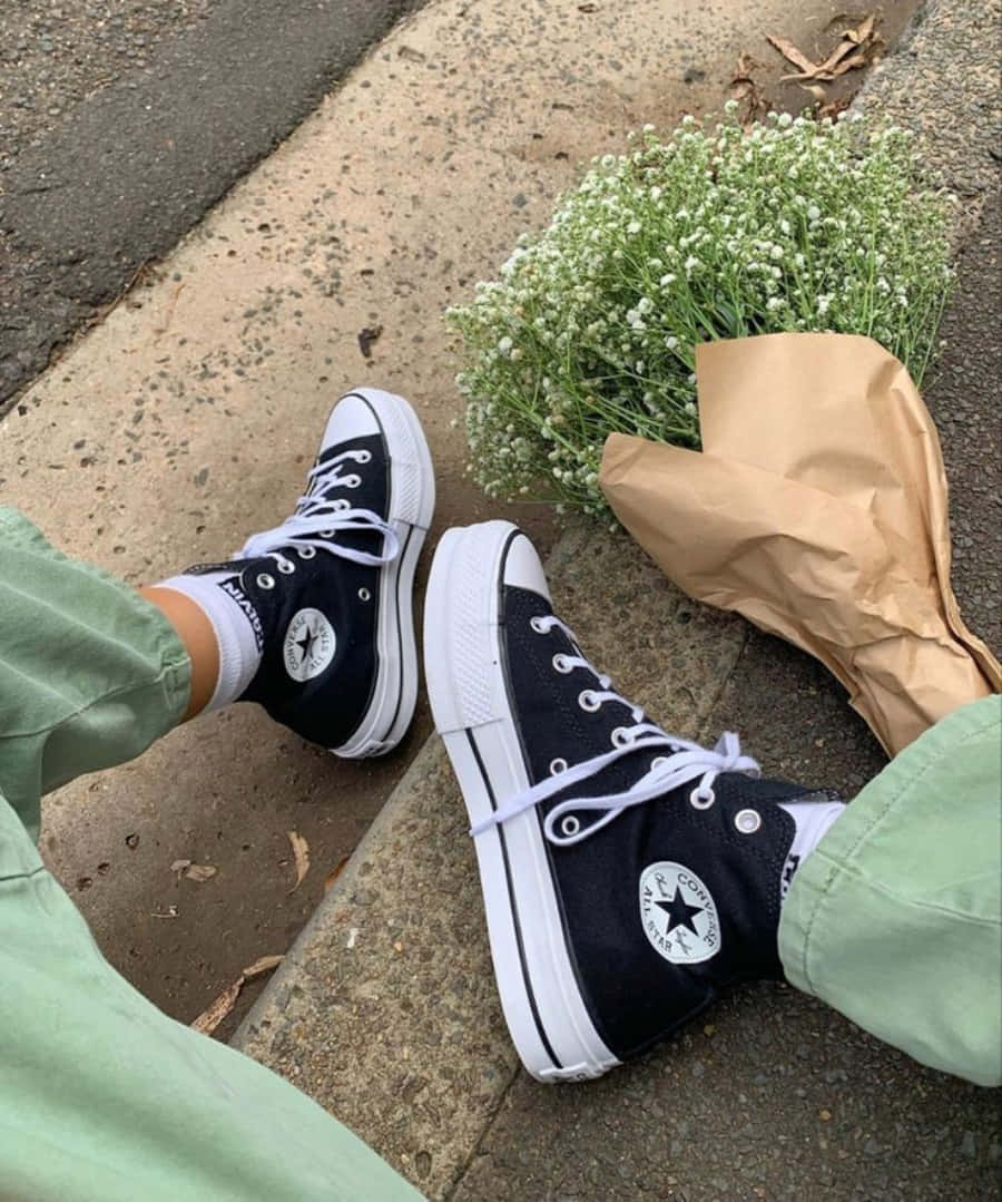 鞋子 桌布 壁紙 — 黑色Converse運動鞋搭配白色鞋帶，旁邊放著一束用紙包裹的滿天星花束，放在人行道上。