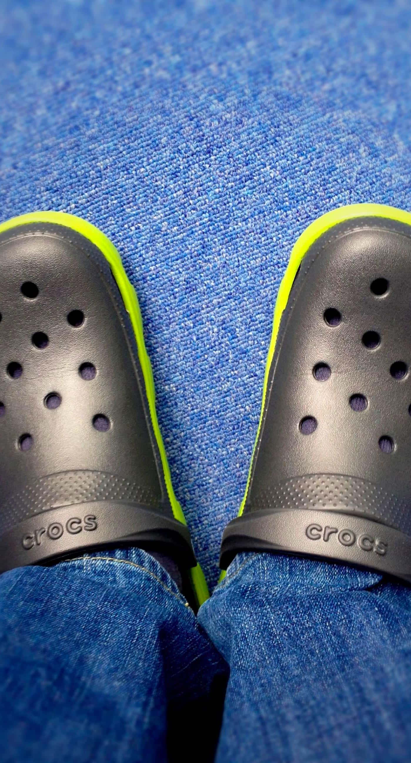 Crocs 桌布 壁紙 — 黑色Crocs配螢光黃飾邊的特寫，放在有紋理的藍色地毯上。