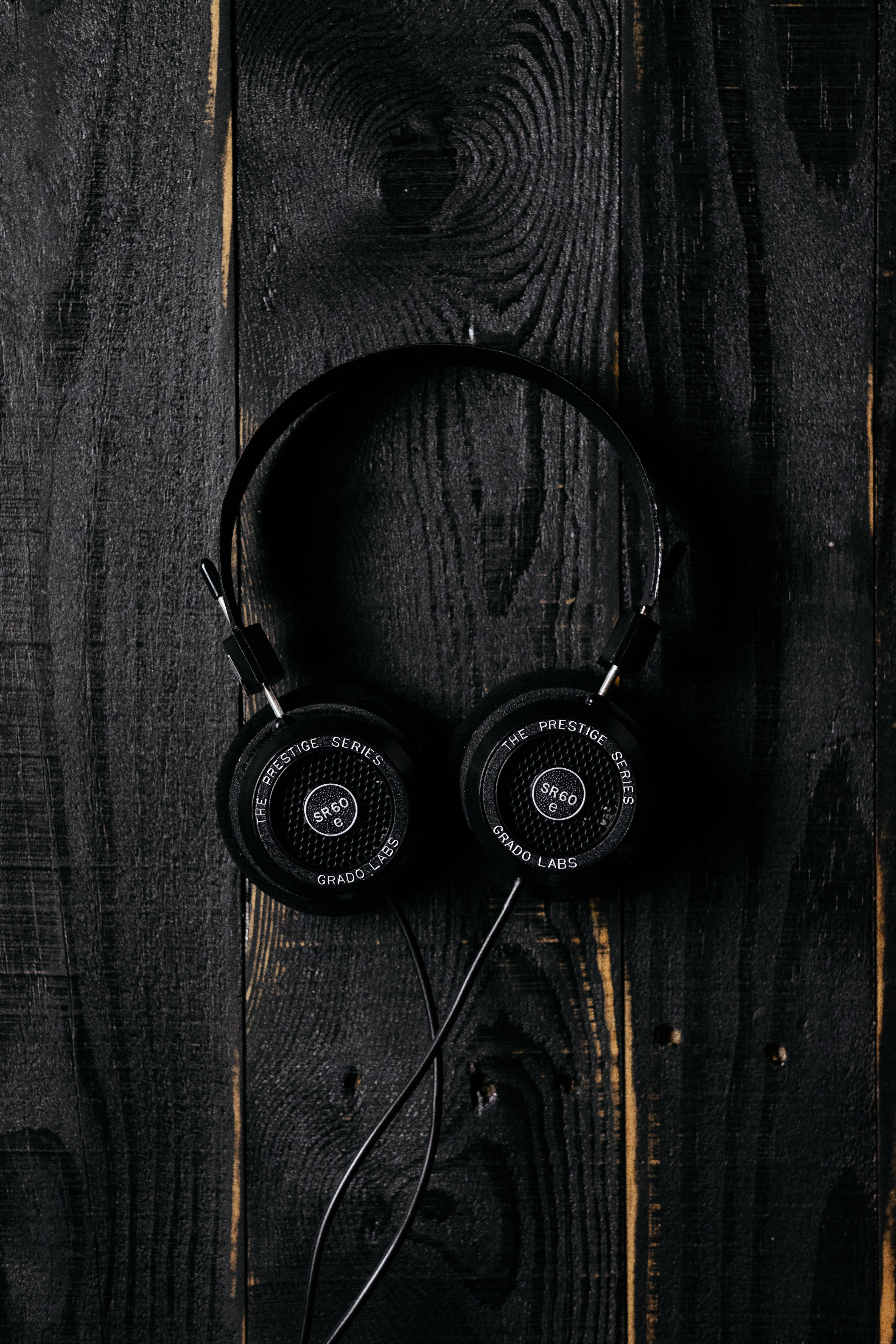 音樂 桌布 壁紙 — 黑色Grado SR60耳機放置在深色紋理木質表面上，帶有可見的木紋和微妙的琥珀色亮點。