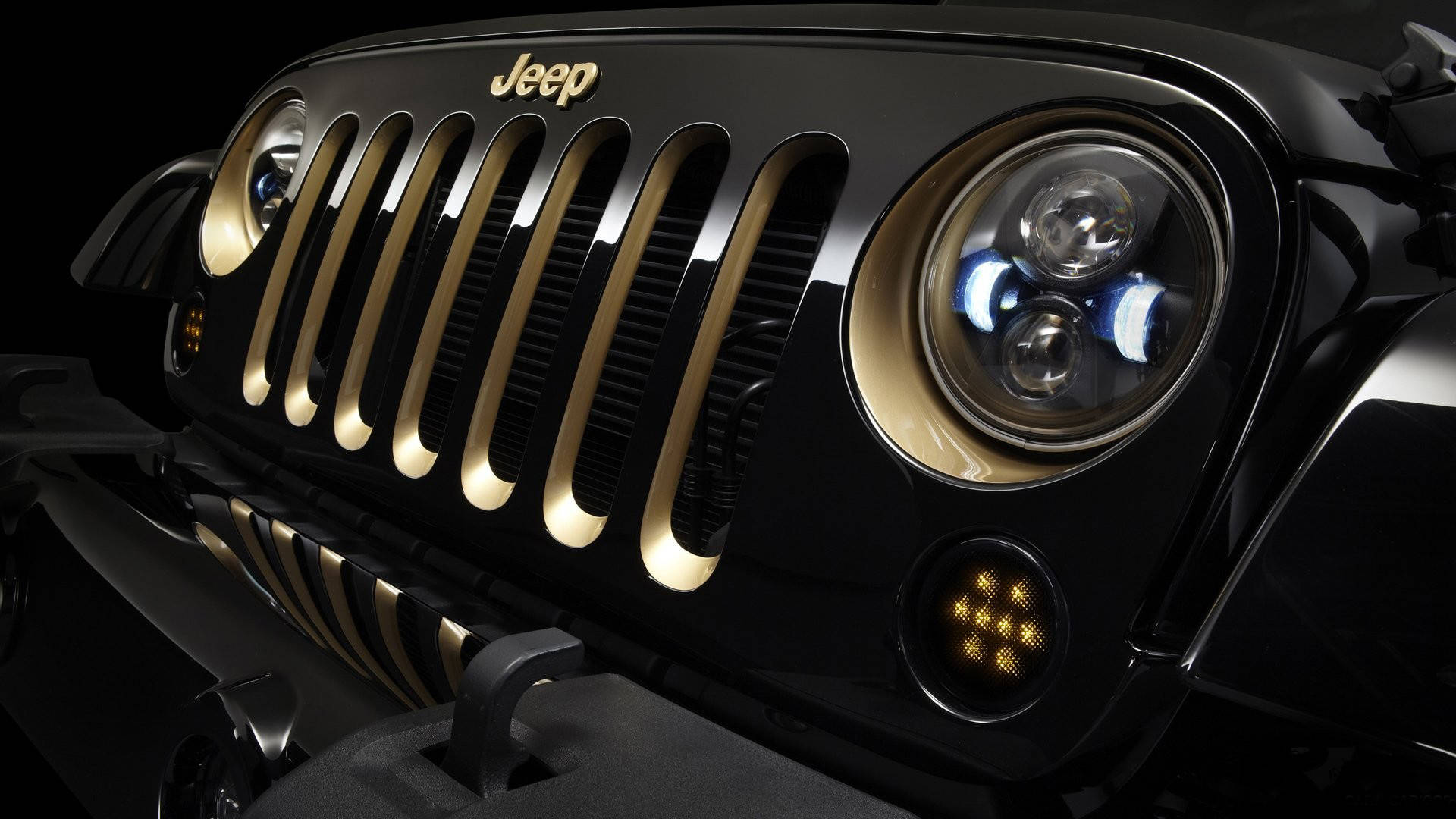 Black Jeep 桌布 壁紙 — 黑色Jeep的前格柵和頭燈特寫，金色裝飾在黑暗背景下發光。