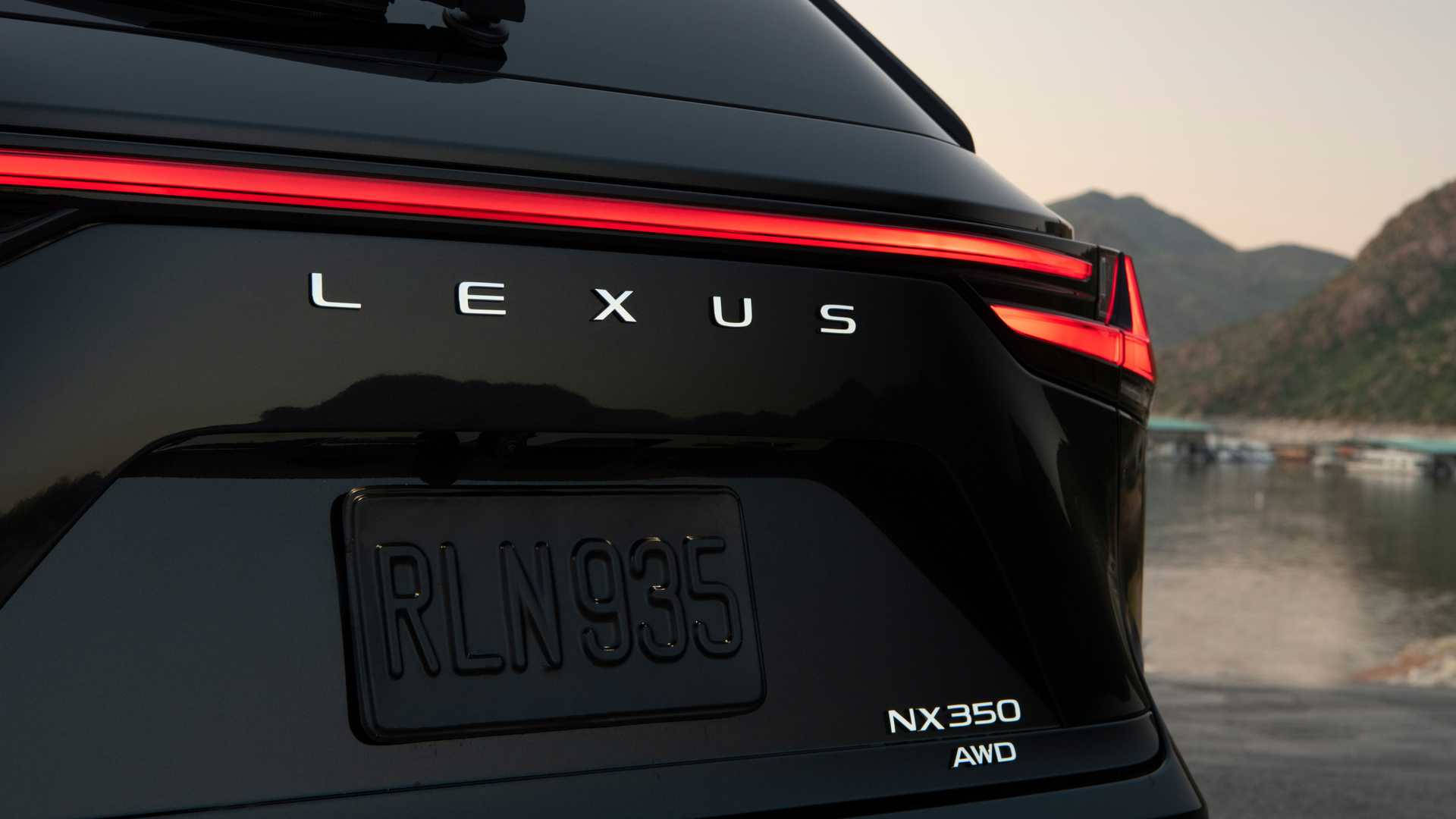 Lexus 標誌 桌布 壁紙 — 黑色Lexus NX 350 AWD車尾特寫，紅色尾燈發光，停泊在黃昏時分的山區海濱。