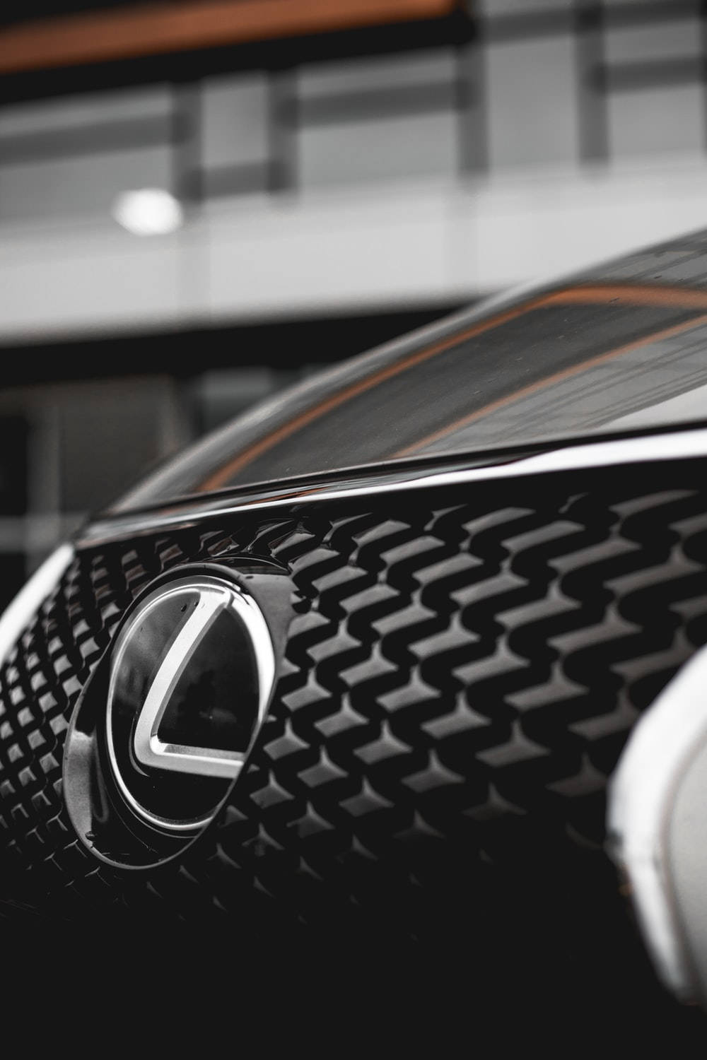 Lexus 標誌 桌布 壁紙 — 黑色Lexus格柵近距離特寫，帶有鍍鉻標誌和橙色飾條，光線柔和。
