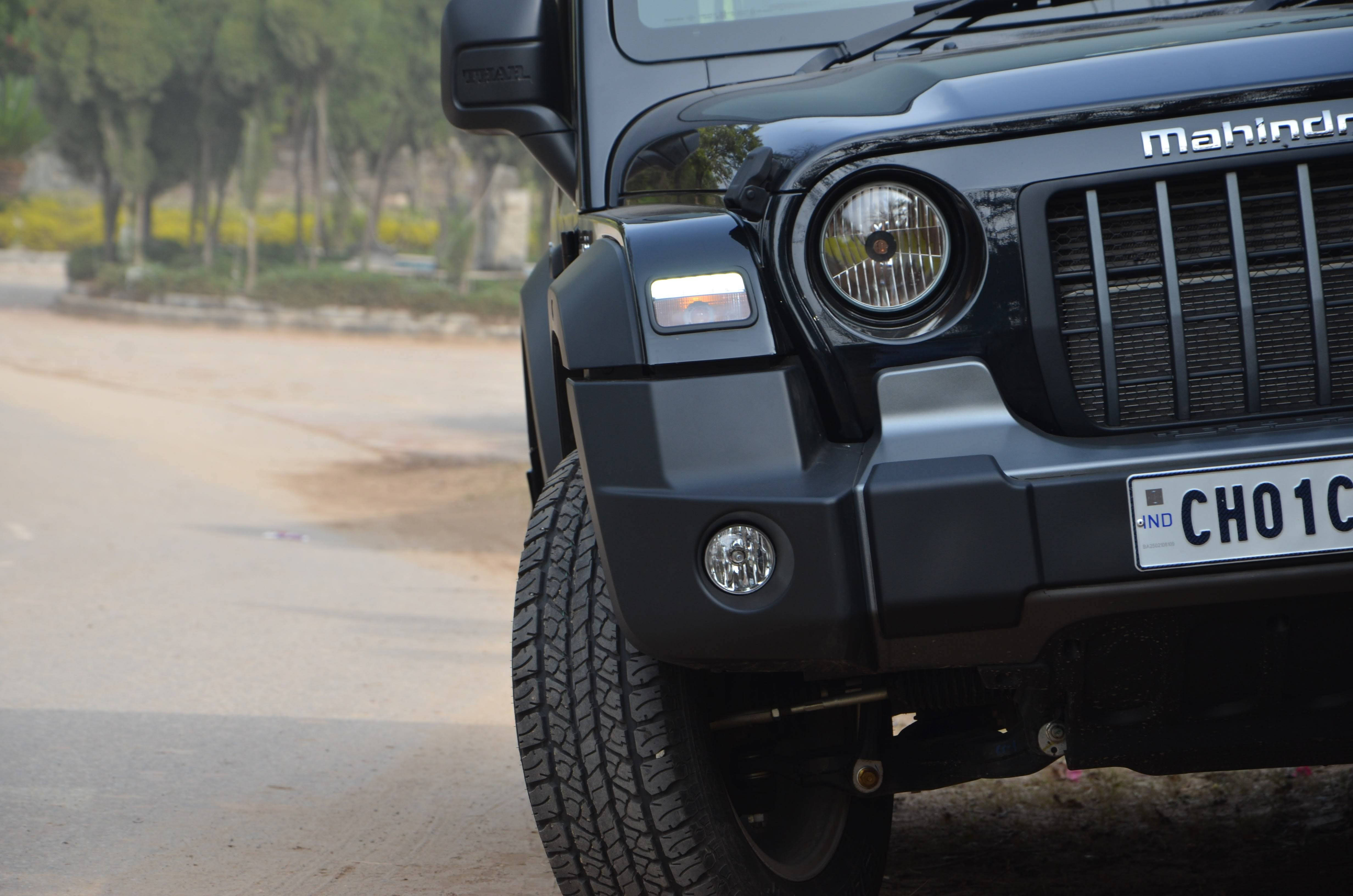 汽車 桌布 壁紙 — 黑色Mahindra Thar SUV在塵土飛揚的道路上，其堅固的前格柵和圓形頭燈的特寫。