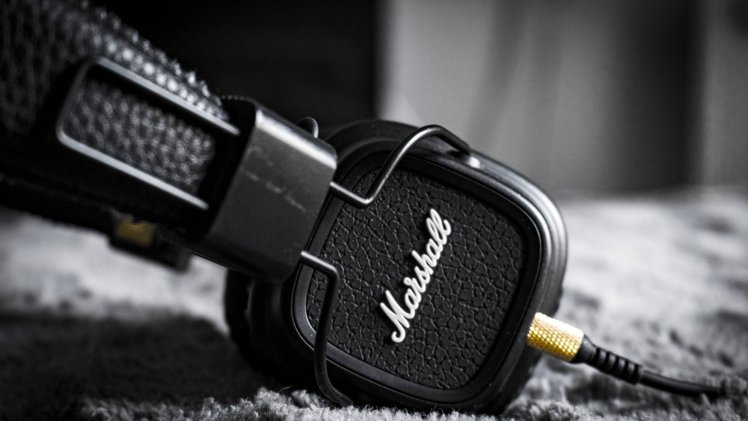 Marshall 桌布 壁紙 — 黑色Marshall耳機特寫，帶金色插頭，放在質感灰色地毯上，單色調。