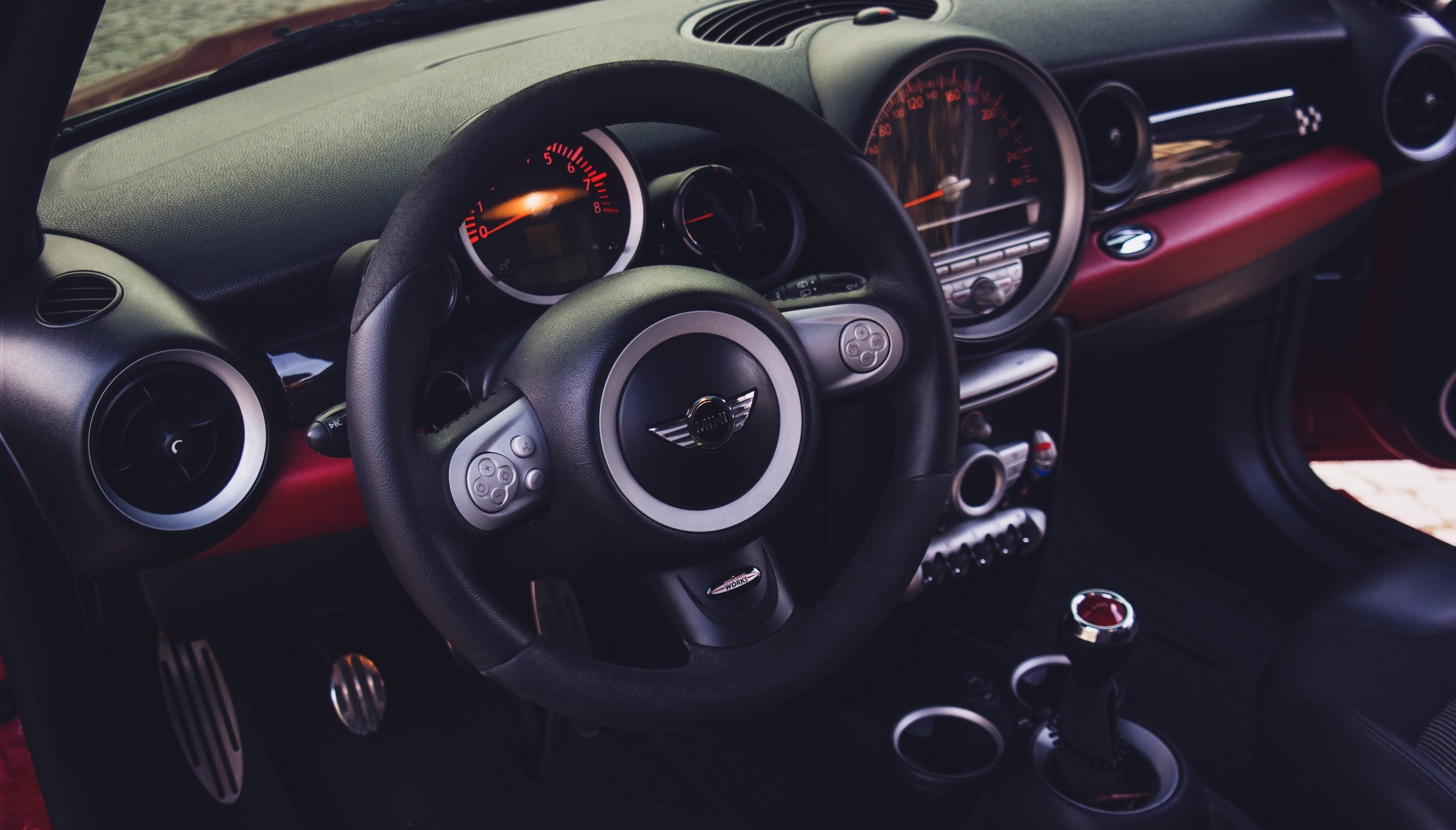 Mini Cooper 桌布 壁紙 — 黑色MINI Cooper車廂內部特寫，帶有紅色點綴和發光的儀表板刻度盤。