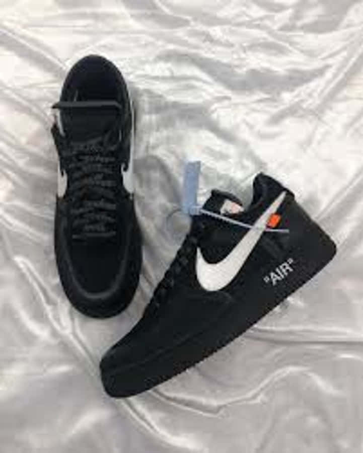 Black Air Force 桌布 壁紙 — 黑色Nike Air Force 1運動鞋，帶白色swoosh和橙色標籤，放在皺巴巴的銀色布料背景上。