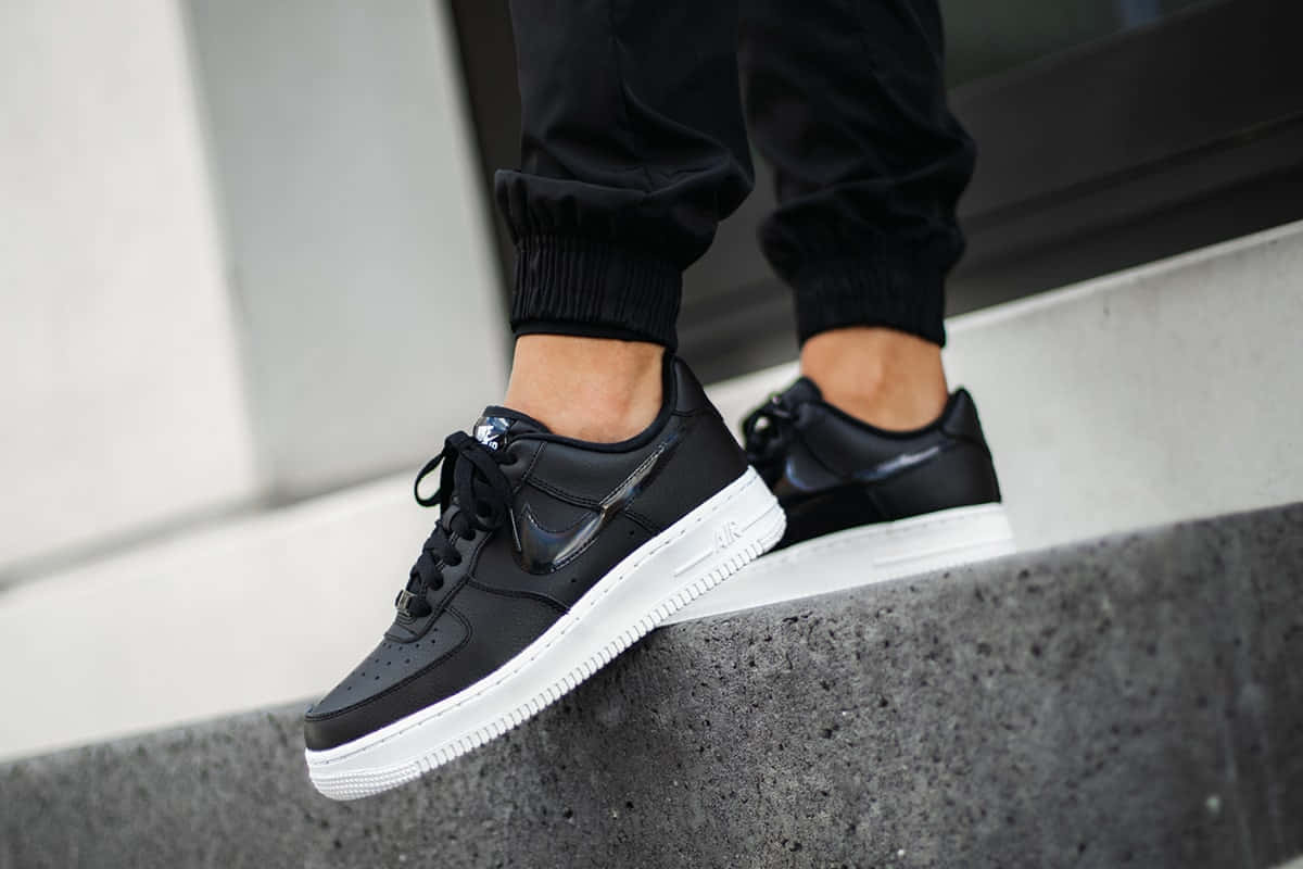 Black Air Force 桌布 壁紙 — 黑色Nike Air Force 1運動鞋白色鞋底的近距離特寫，由站在混凝土邊緣的人穿著。
