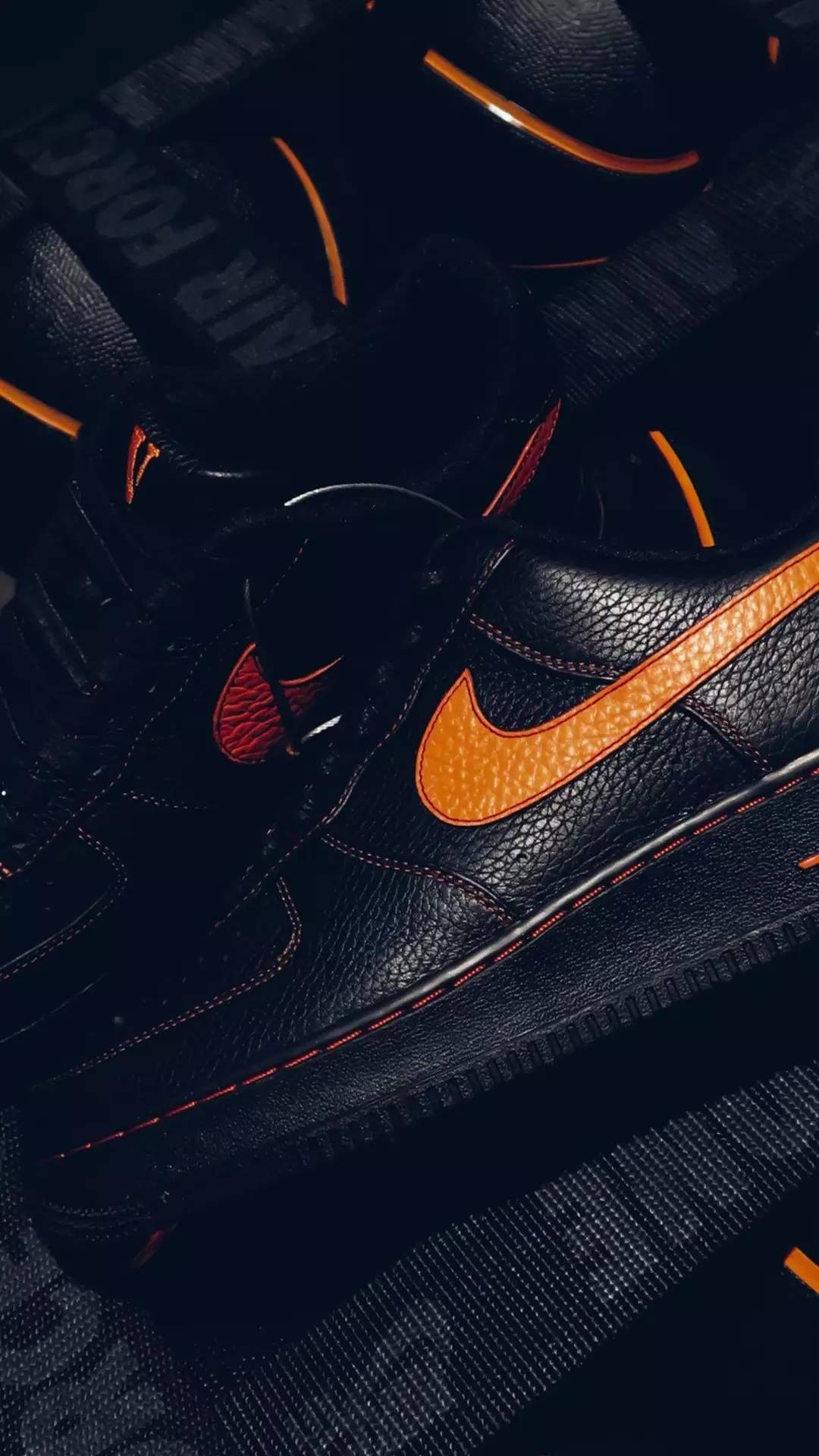 Vlone 桌布 壁紙 — 黑色Nike Air Force 1運動鞋特寫，帶有醒目橙色點綴和紅色縫線，在戲劇性燈光下拍攝。