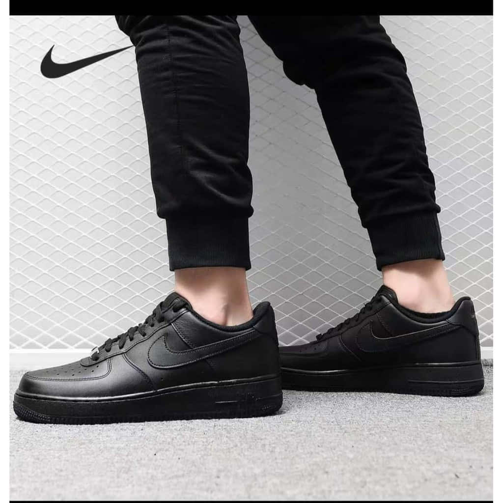 Black Air Force 桌布 壁紙 — 黑色Nike Air Force 1運動鞋搭配黑色慢跑褲，白色瓷磚牆背景的特寫。