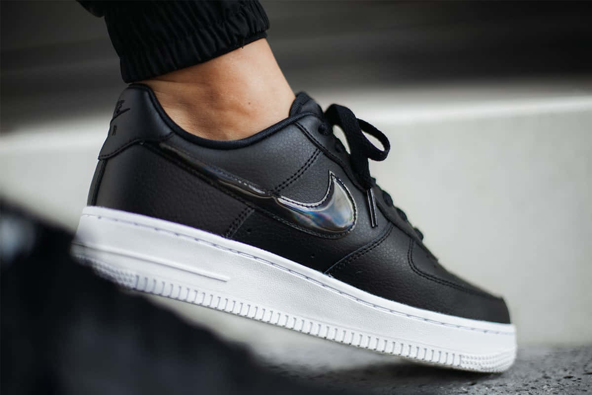 Black Air Force 桌布 壁紙 — 黑色Nike Air Force 1運動鞋特寫，鞋身帶有全息Swoosh標誌，置於混凝土階梯上。