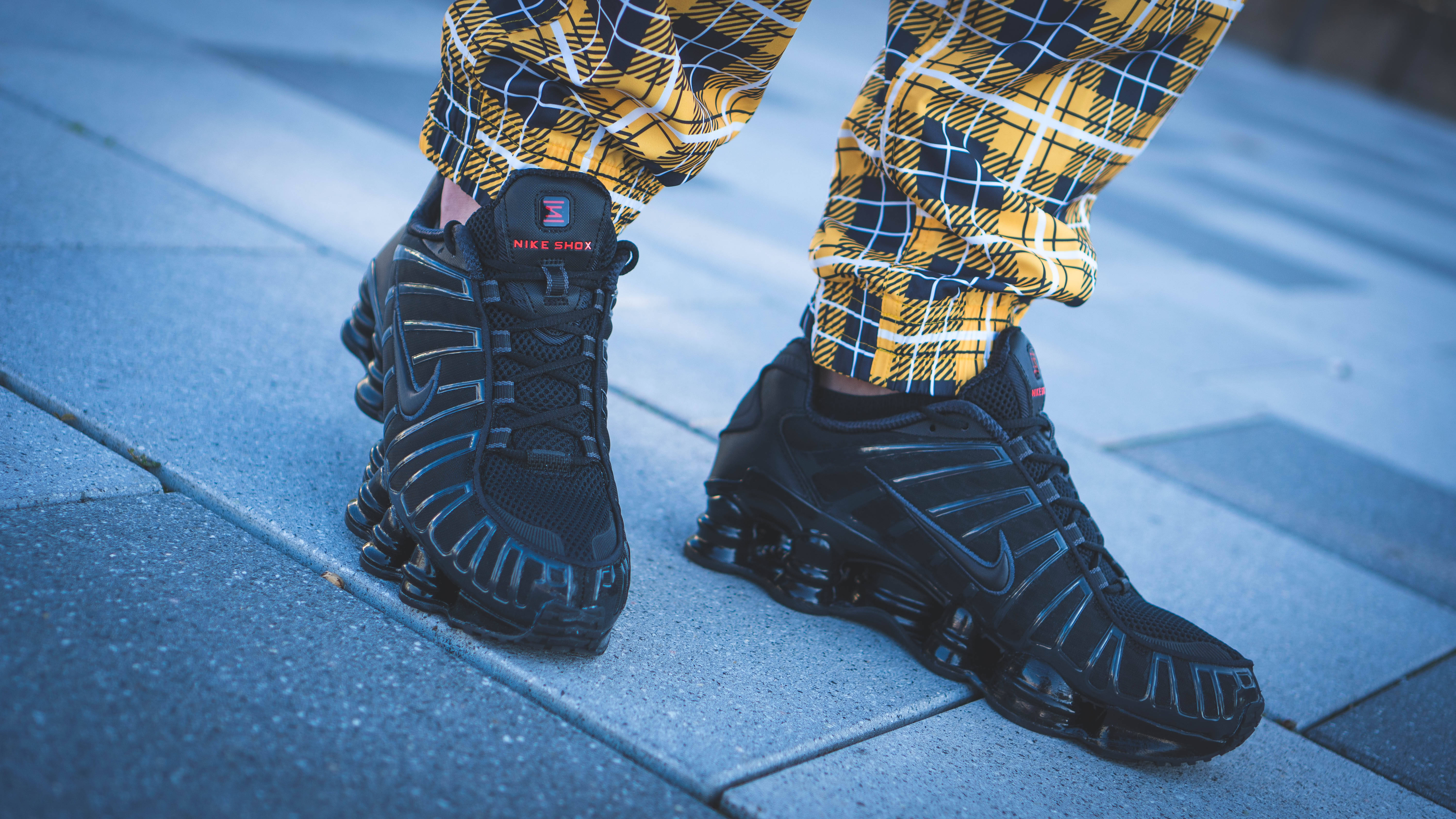 Checkered 桌布 壁紙 — 黑色Nike Shox運動鞋搭配黃色格紋褲在藍色調人行道上的特寫。