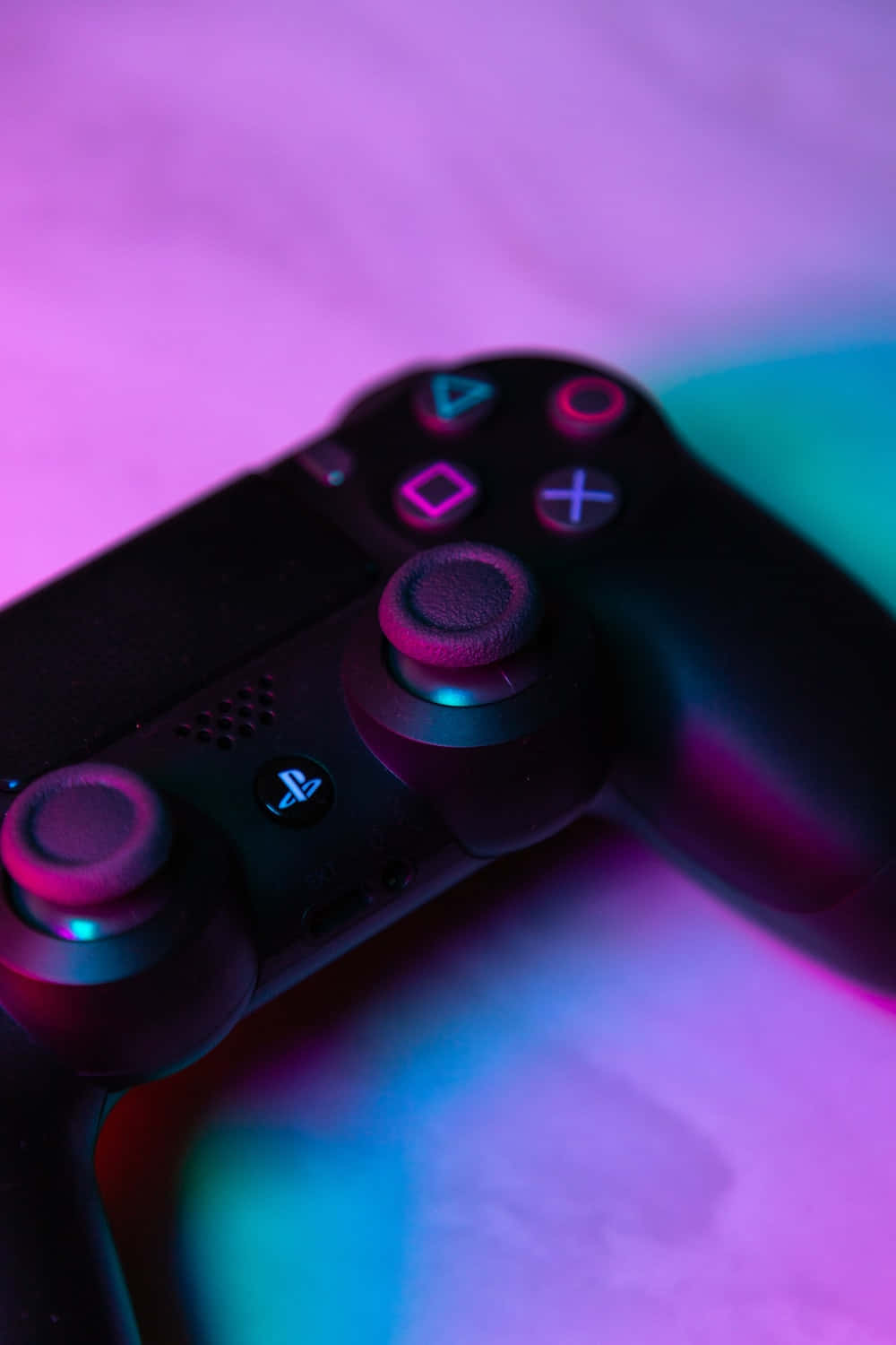 PlayStation 桌布 壁紙 — 黑色PlayStation控制器在柔軟表面上被鮮豔的粉紅和青色霓虹燈照射的特寫。