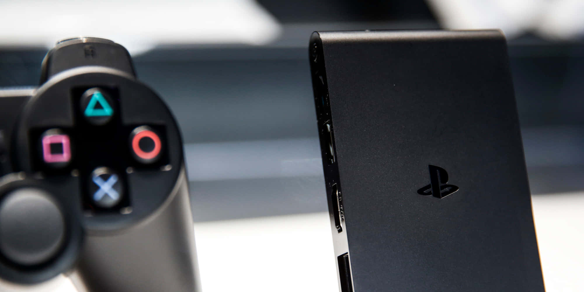 PlayStation 桌布 壁紙 — 黑色PlayStation控制器和主機的特寫，帶有發光的彩色按鈕和時尚的啞光飾面。