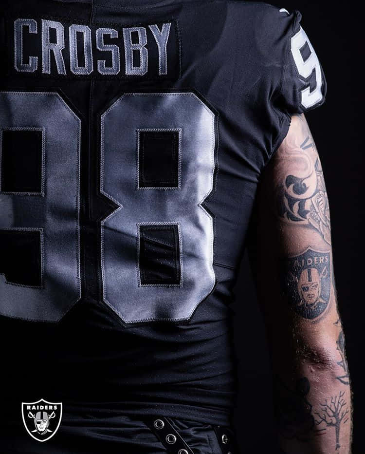 Las Vegas Raiders 桌布 壁紙 — 黑色Raiders足球球衣特寫，號碼98和名字Crosby，顯示有刺青的手臂，背景深色。