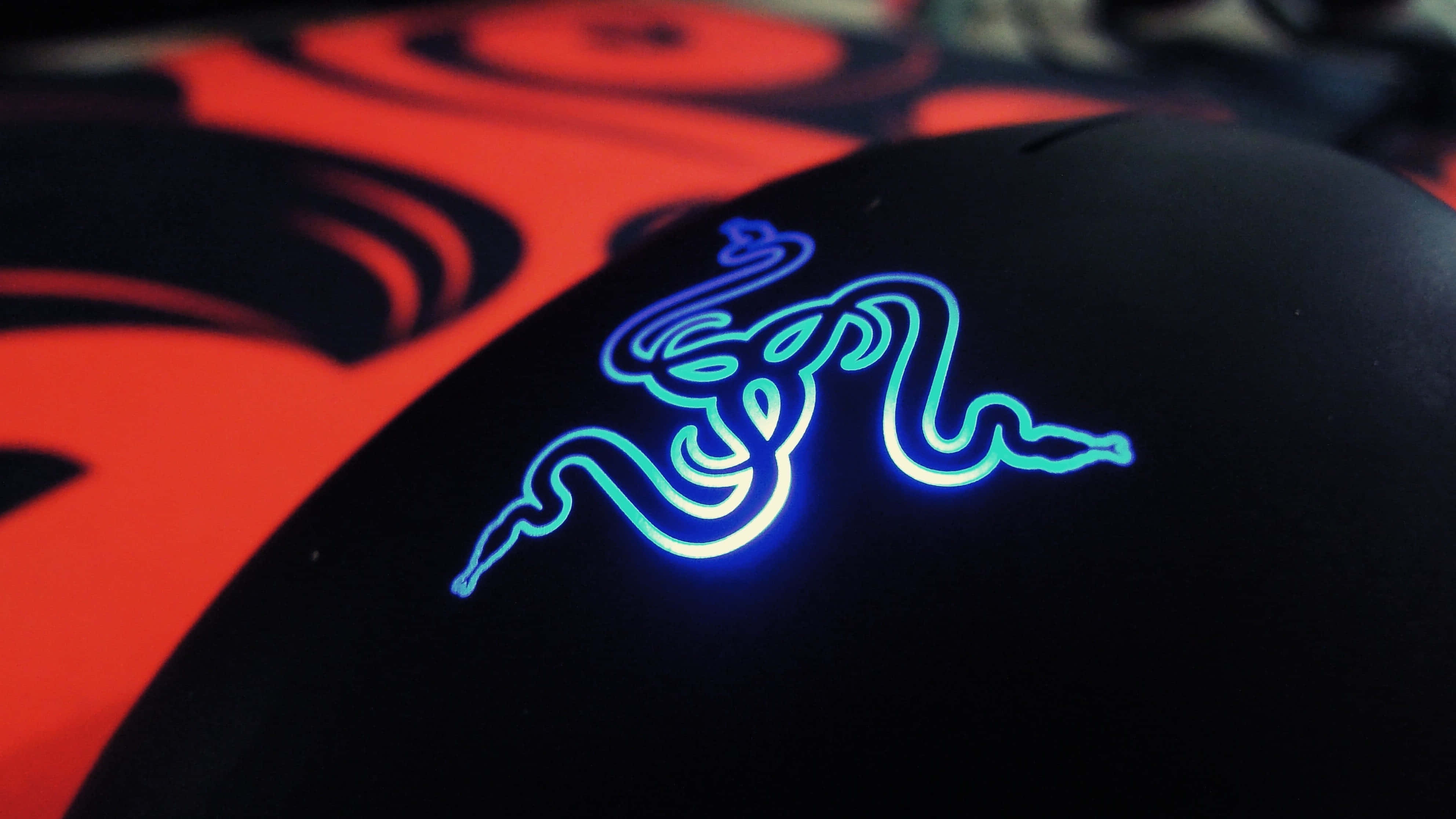 Gaming Mouse 桌布 壁紙 — 黑色Razer滑鼠特寫，帶有發光藍色標誌，背景為紅色和黑色漩渦。
