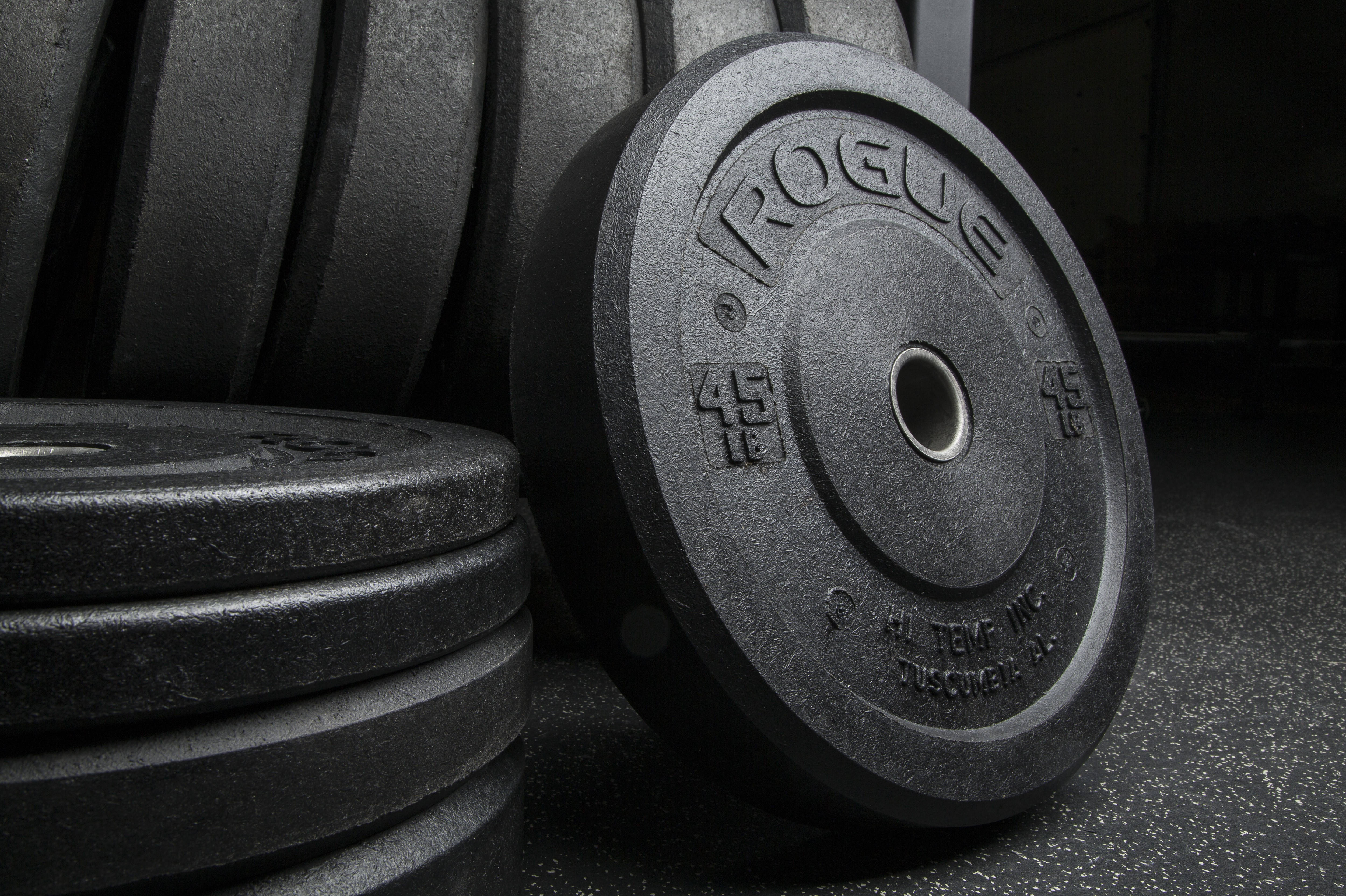 Barbell 桌布 壁紙 — 黑色Rogue 45磅槓鈴片特寫，旁邊是疊起的健身槓鈴片，放在橡膠地板上。