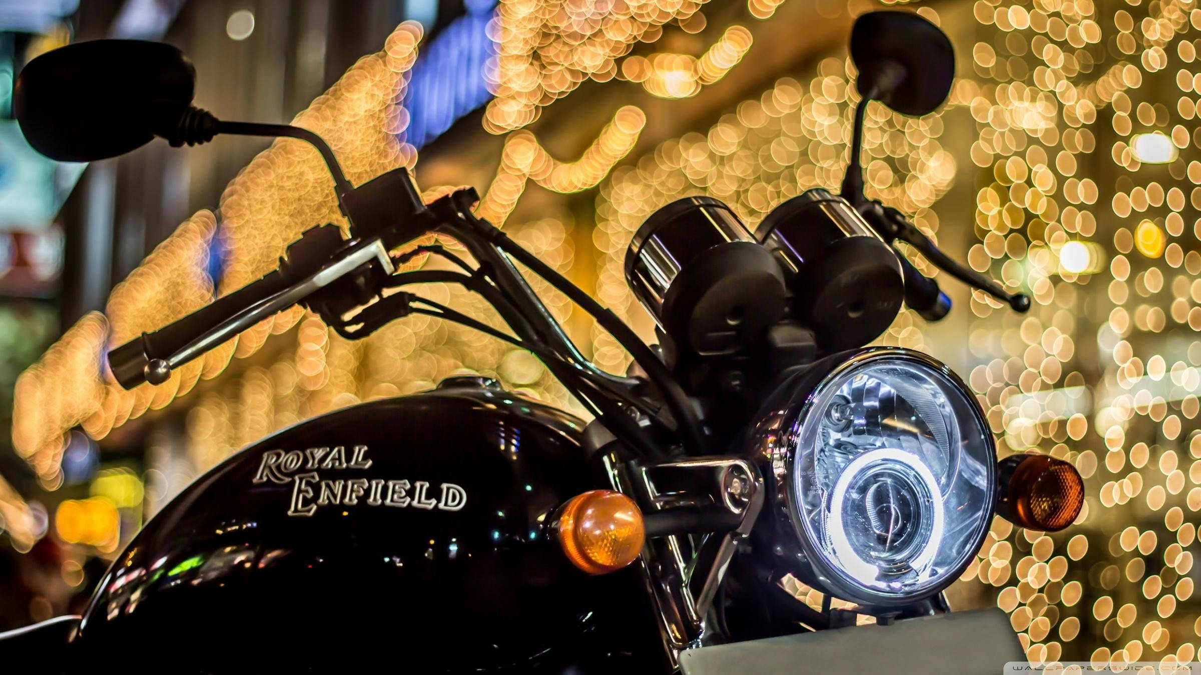 Royal 桌布 壁紙 — 黑色Royal Enfield機車頭燈在夜間金色城市燈光的生動散景中發光的特寫。
