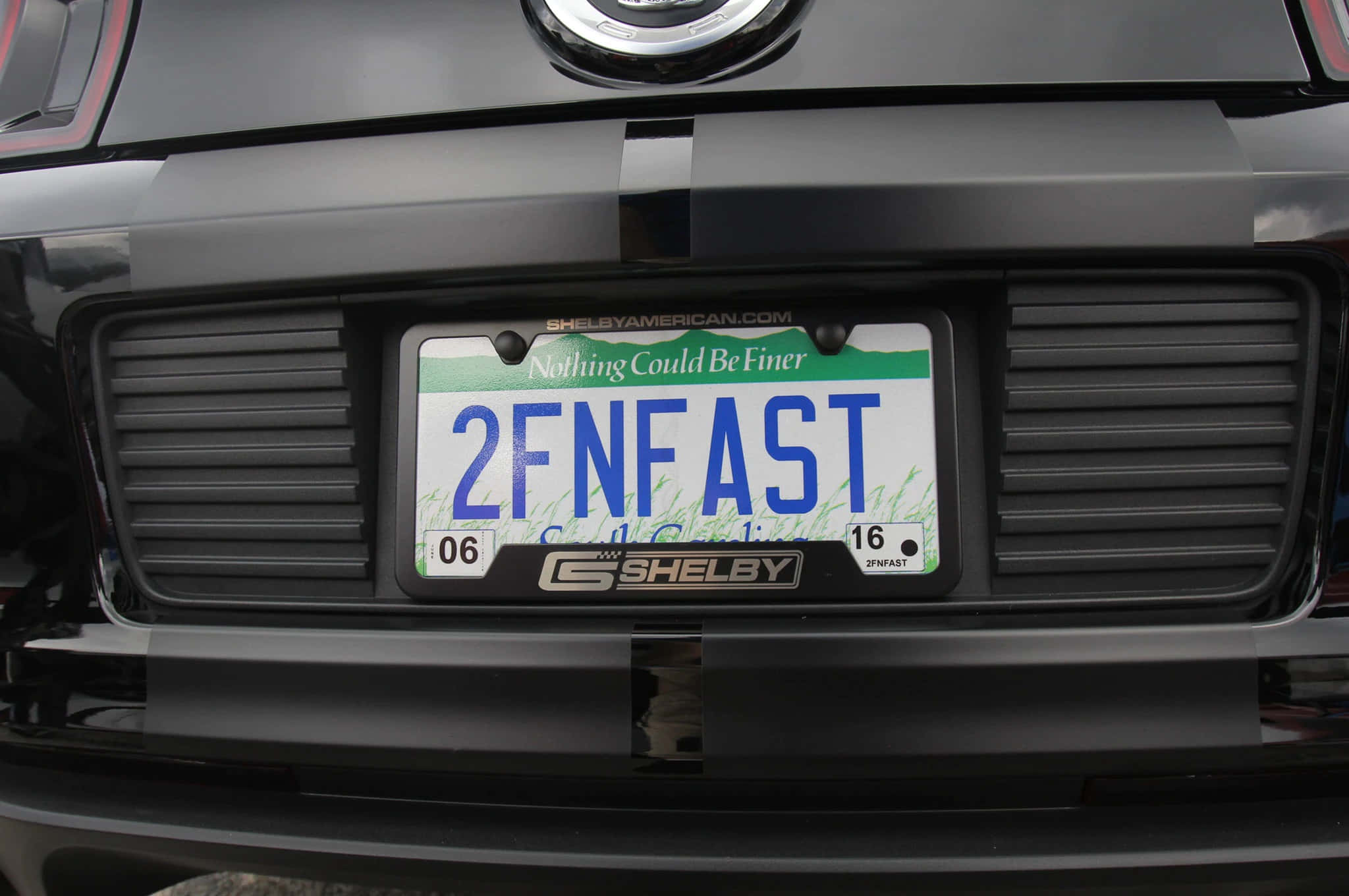 Car License Plate 桌布 壁紙 — 黑色Shelby車尾特寫，自訂車牌上寫著2FNFAST，帶有草地設計和標語「Nothing Could Be Finer」。