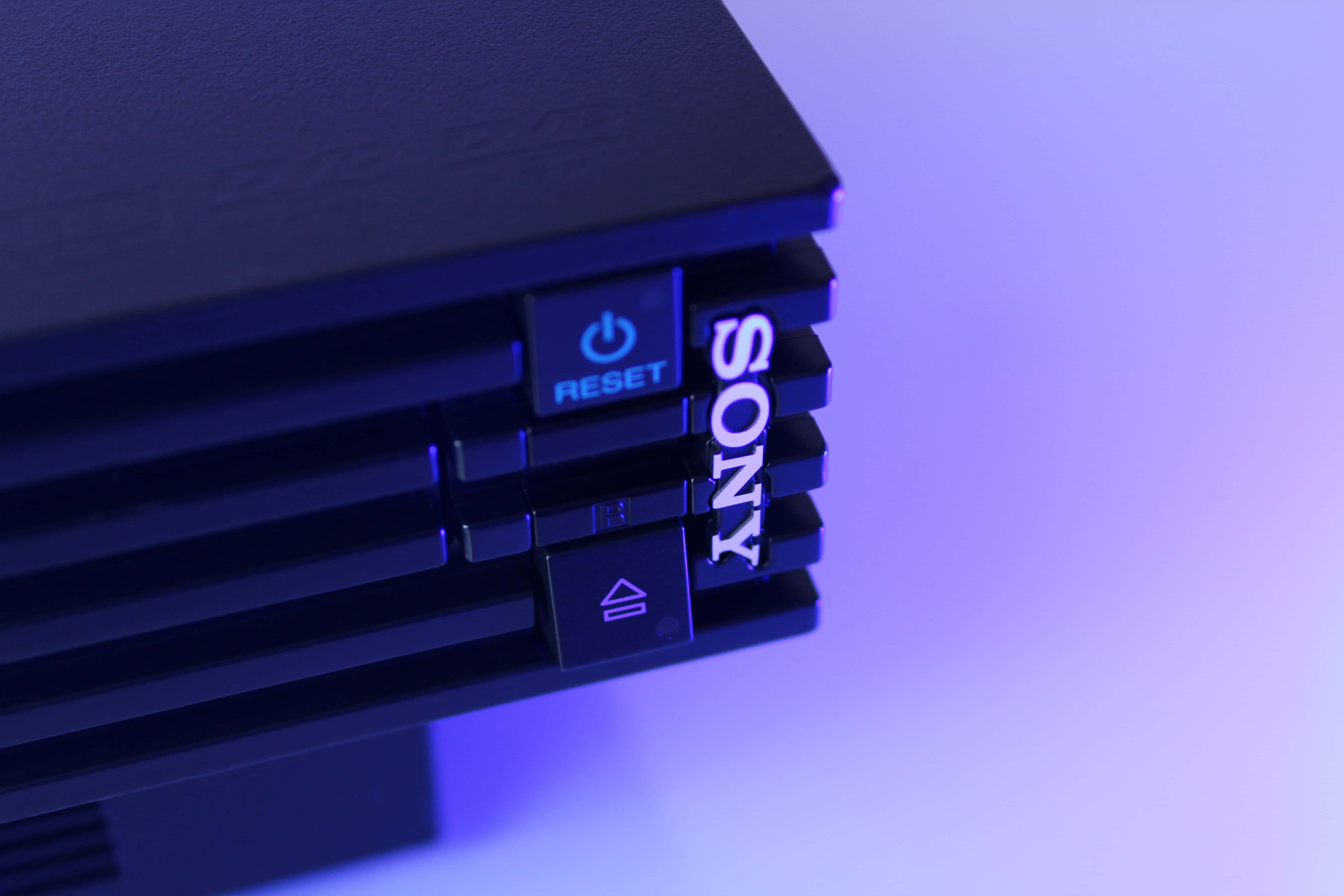 Gaming Consoles 桌布 壁紙 — 黑色Sony PlayStation主機特寫，帶有發光藍色重置按鈕和標誌，背景為柔和紫色漸變。